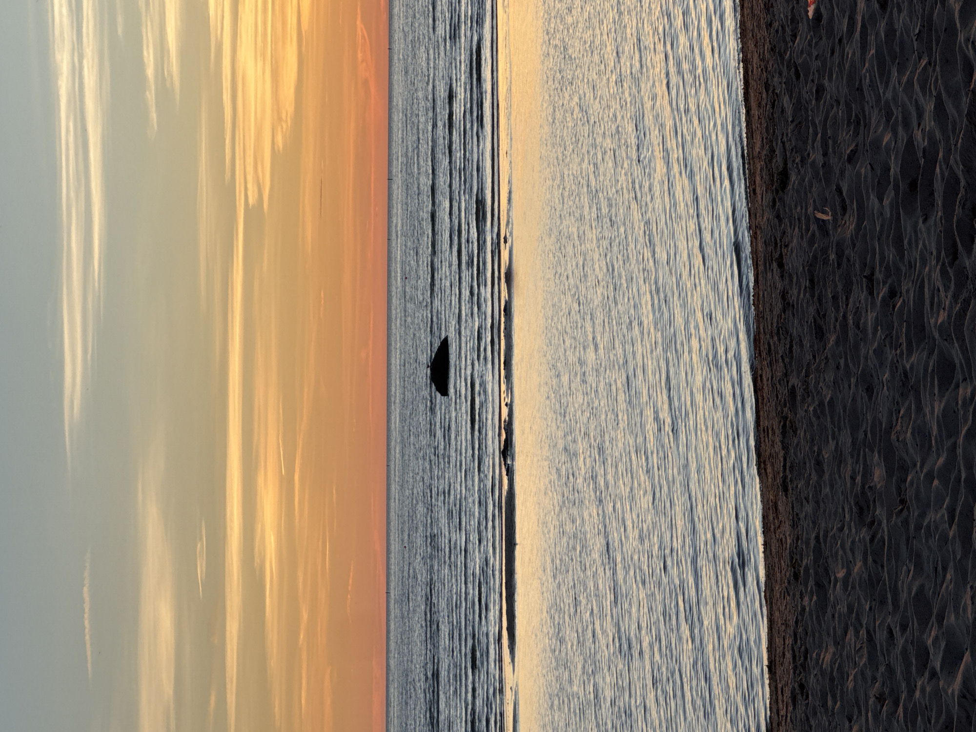 The image depicts a serene sunset over the Baltic Sea, with a sandy beach in the foreground. The sky is a canvas of warm hues, transitioning from a pale blue at the top to vibrant orange and yellow streaks near the horizon, indicative of a sunset. Wispy clouds are scattered across the sky.
The sea is calm, with gentle ripples on its surface. A dark, solitary rock is visible in the middle distance, emerging from the water. Further out, the horizon line is clearly defined, separating the sea from the sky. In the immediate foreground, a sandy beach with subtle undulations is visible, suggesting the texture of the sand. The overall impression is one of tranquility and natural beauty.
Without further context or visual cues, it is not possible to pinpoint the exact location within Tallinn, Estonia. However, the scene is consistent with coastal areas in and around the city that border the Baltic Sea, such as the beaches of Pirita or other areas along the northern coastline.