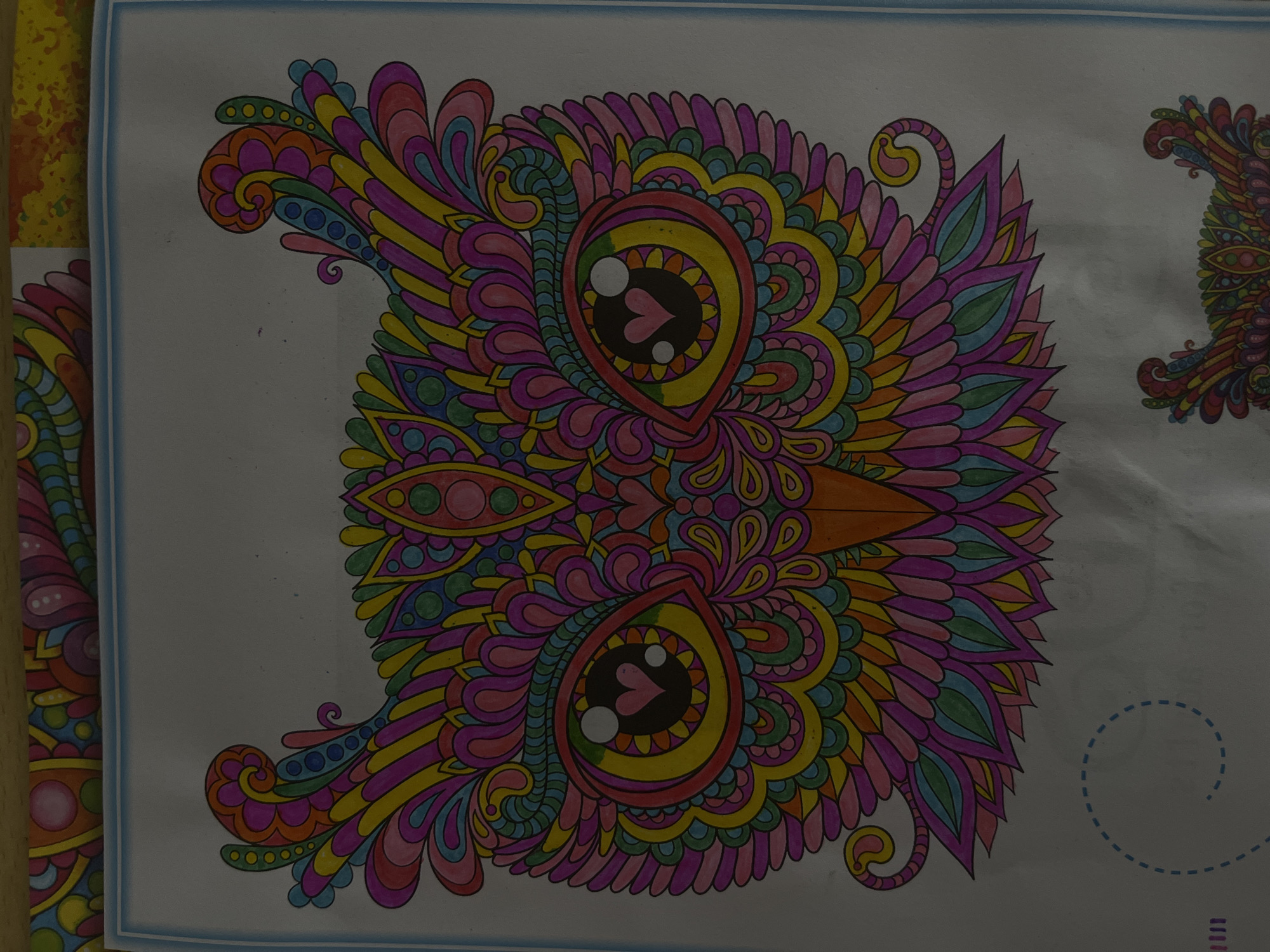 The image depicts a colorful, stylized owl drawing. The owl is rendered in a variety of vibrant colors, including pink, yellow, green, and orange. The design features intricate paisley-like patterns and decorative elements filling the owl's form. The eyes of the owl are large and teardrop-shaped, with heart-shaped pupils. The background is white. The image is part of a coloring book or illustration. There is no information to suggest the image is related to Maladzyechna, Belarus.
