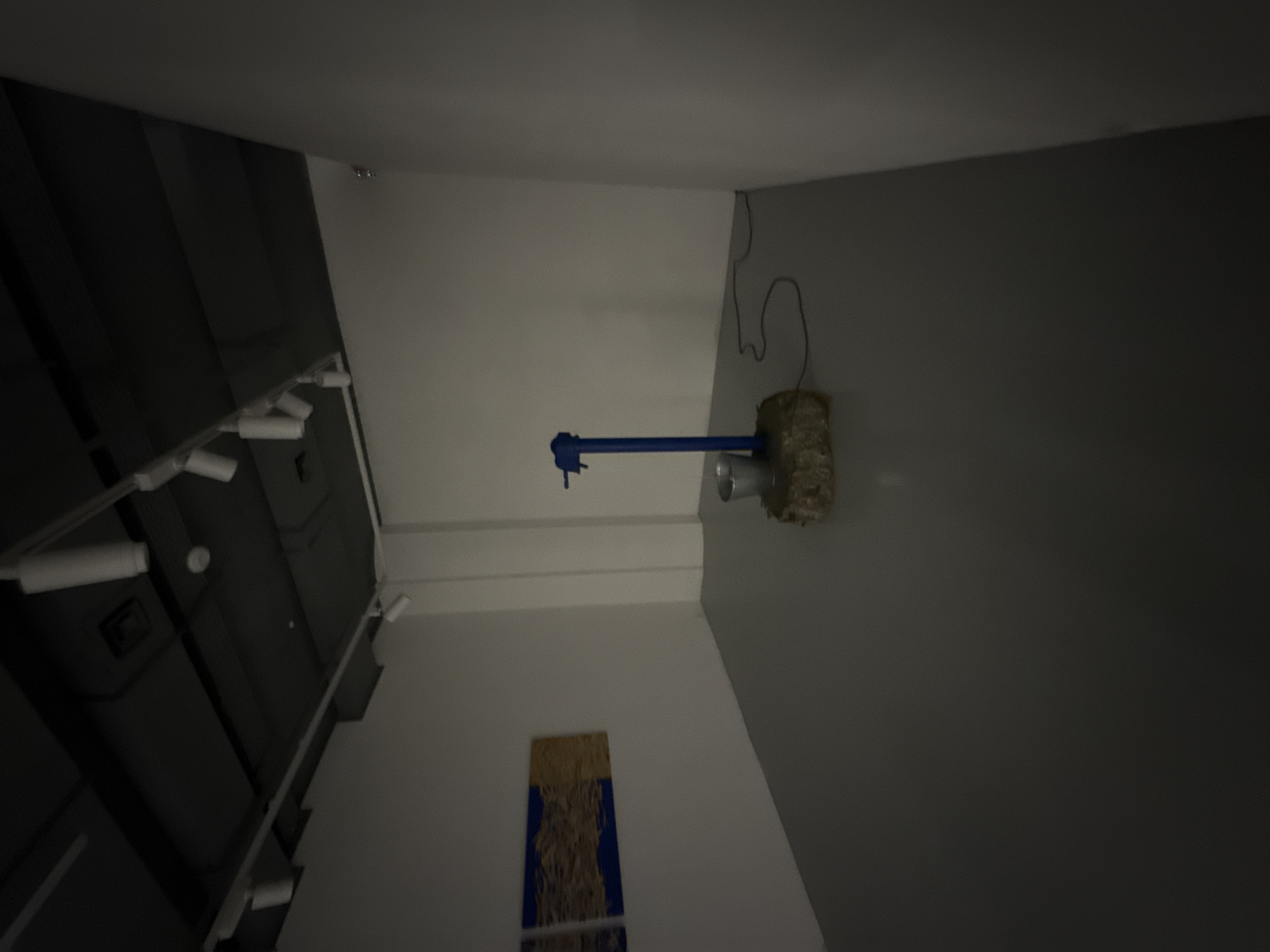 The image shows an indoor scene with various elements. On the left, there is a ceiling with recessed lighting. The right side of the image is a gray wall, on which a blue and gray pipe-like structure is mounted. There is also some electrical wiring visible on the right wall. A rectangular wall hanging with gold and blue patterns can be seen toward the bottom left. The location, Moscow, Russia, is not discernible from the image provided.