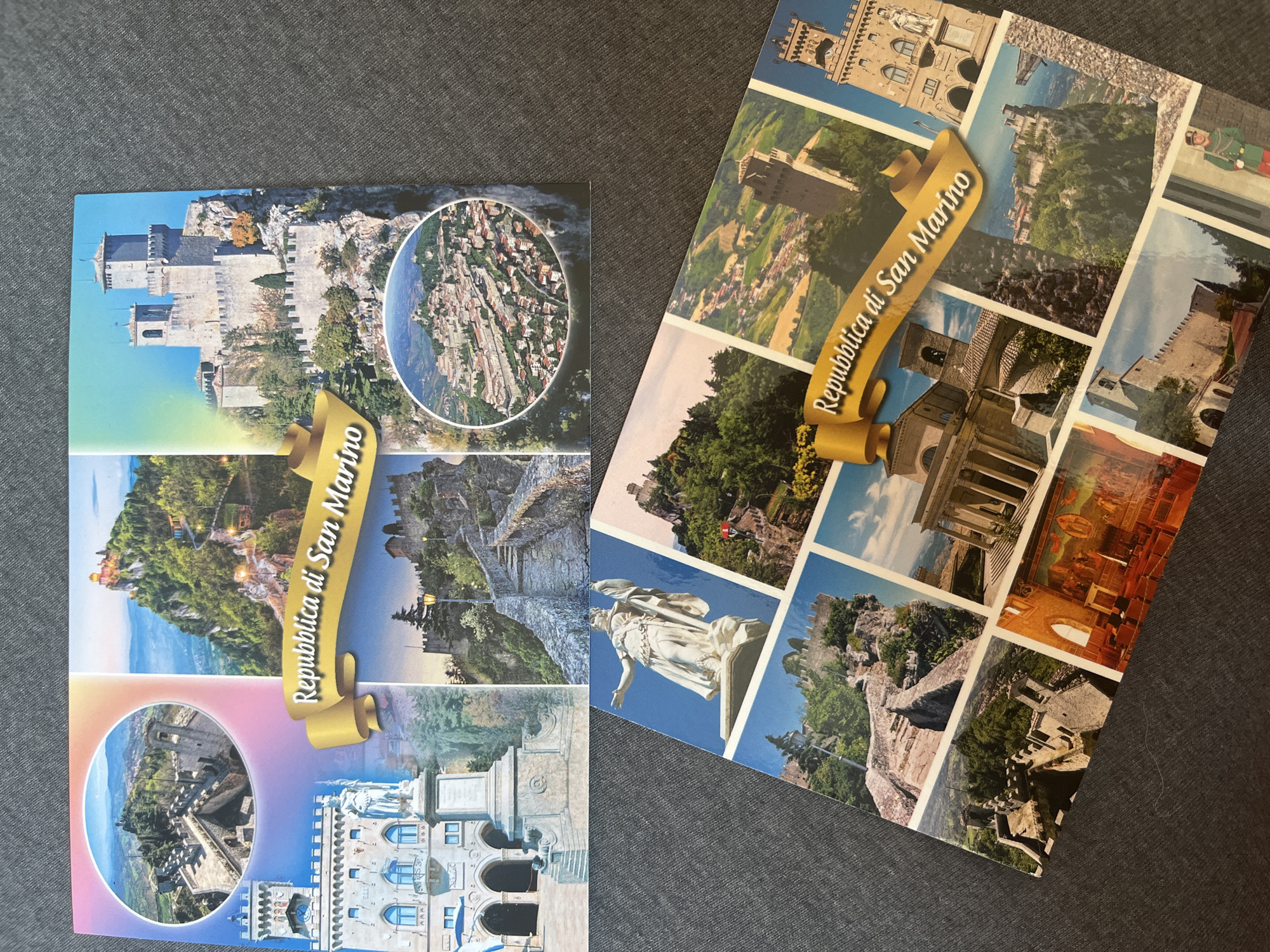 The image displays two San Marino postcards. The top postcard features a montage of San Marino landmarks. The top left shows the first tower of San Marino, "Guaita", with walls and a courtyard. To its right is a view of the third tower, "Montale", perched on a rocky outcrop, and a winding path illuminated by streetlights. The bottom left showcases the Palazzo Pubblico (Town Hall) with a statue in front. The bottom right shows a close-up of a stone staircase leading up to a castle, with a street lamp. A circular inset in the top right provides an aerial view of the historic city of San Marino. A golden banner across the center reads "Repubblica di San Marino".
The bottom postcard also presents a collection of San Marino scenes. A prominent statue of a woman holding a flag is visible in the upper left. Other images include various towers, stone structures, pathways, and a fresco. The same golden banner with "Repubblica di San Marino" is present.
There are no people visible in the top postcard. The bottom postcard has a figure in a green uniform with a red sash and hat in the lower right corner.
The scene is not located in Montana, Bulgaria. It depicts San Marino, an independent microstate enclaved within Italy.