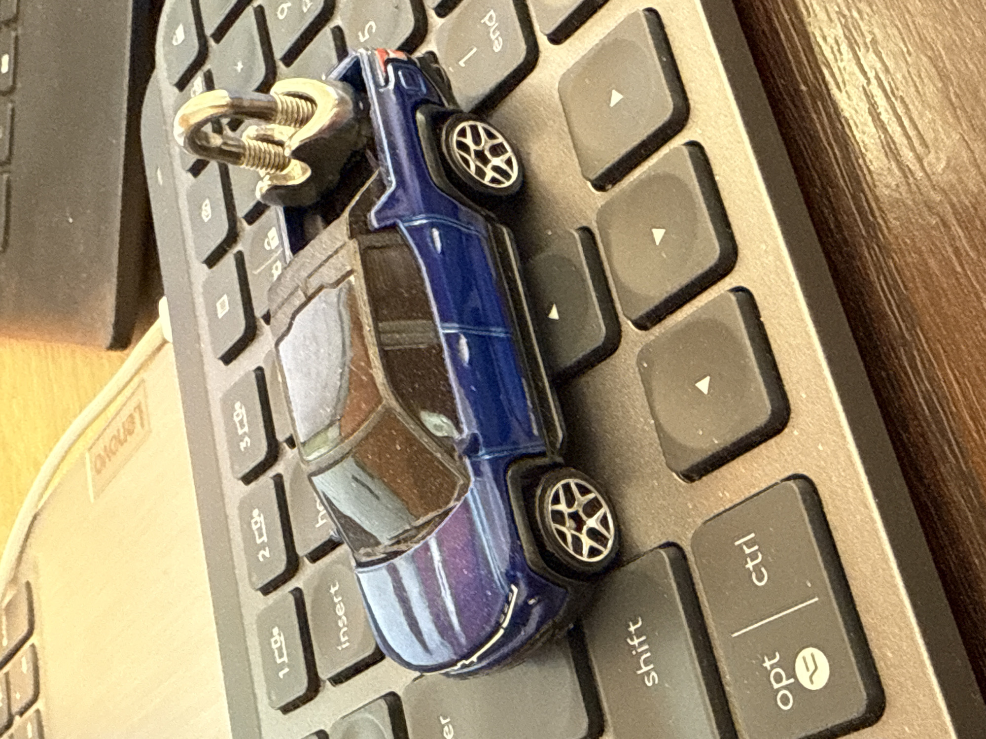 A blue toy car with a keychain is resting on a gray laptop keyboard. The "shift", "ctrl" and "opt" keys are visible. A small part of a Lenovo laptop is also visible. The image does not depict Šušanj, Montenegro, and lacks information about people, actions, or interactions.