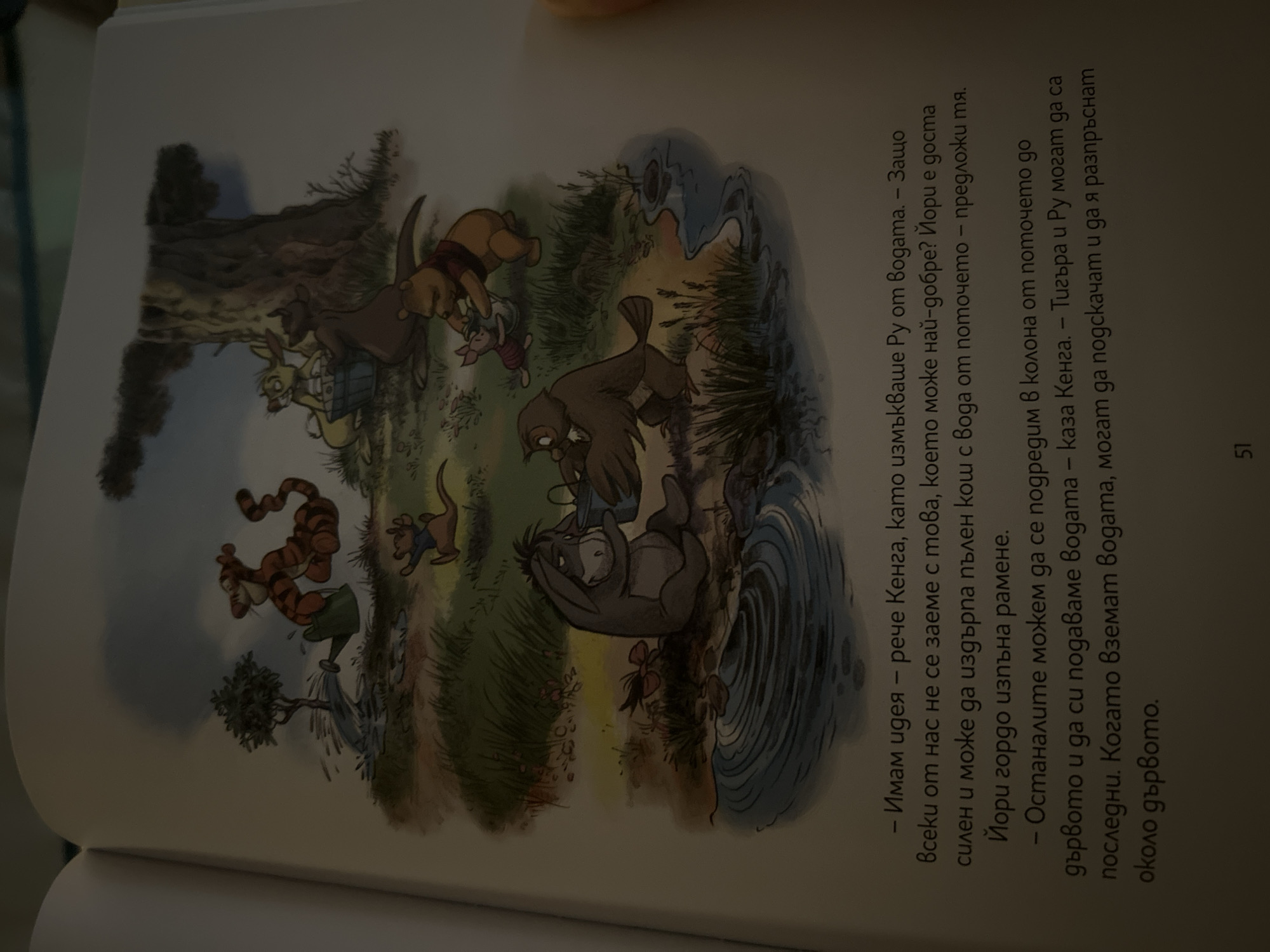 The image shows an illustration from a children's book featuring characters from Winnie the Pooh. In the foreground, Eeyore is sitting by a body of water, holding a bucket. Piglet and Pooh are near a tree, with Pooh appearing to help Piglet with a bucket. An owl character is also present in the foreground. In the background, Tigger is watering a small tree with a watering can, and Kanga and Roo are near a large tree, with Roo in a bucket. The scene depicts a natural outdoor environment with trees, grass, and water. There is text in Bulgarian below the illustration, including a page number "51" at the bottom. The image is a photograph of a page from a book, likely taken in a home or library. There is no information in the image that suggests a location in Sofia, Bulgaria.