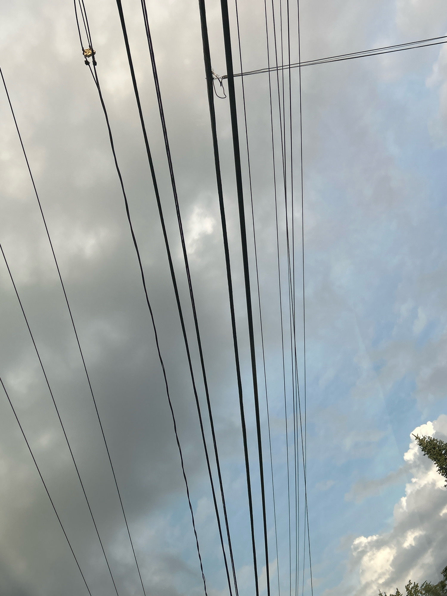 The image shows a view of telephone wires against a sky with clouds. The wires are stretched diagonally across the frame, with some wires thicker than others. The sky is a mix of gray and blue, with patches of white clouds visible. The lighting suggests it is daytime, possibly overcast or late afternoon. The scene appears to be outdoors, with a hint of green foliage visible at the bottom right corner. No people or specific landmarks are discernible in the image. The location is identified as Robinson Township, United States of America, though this specific location is not visually evident within the image itself.