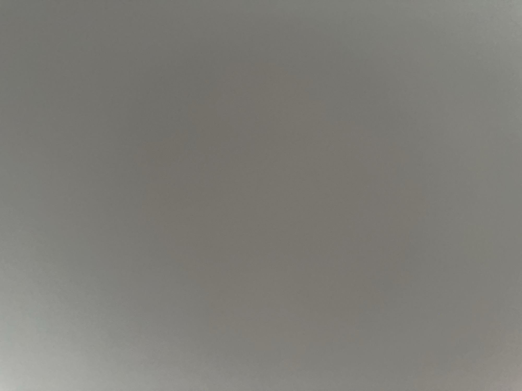 The image is a close-up, abstract shot of a plain, gray, textured surface. There are no discernible subjects, objects, or scenes. No activity or event is taking place. The image is uniformly gray with subtle variations in lighting that create a soft gradient effect. The texture appears to be that of a slightly rough surface, possibly fabric or a painted wall. No time of day, weather, location cues, or emotions are evident. There is no visible text in the image.