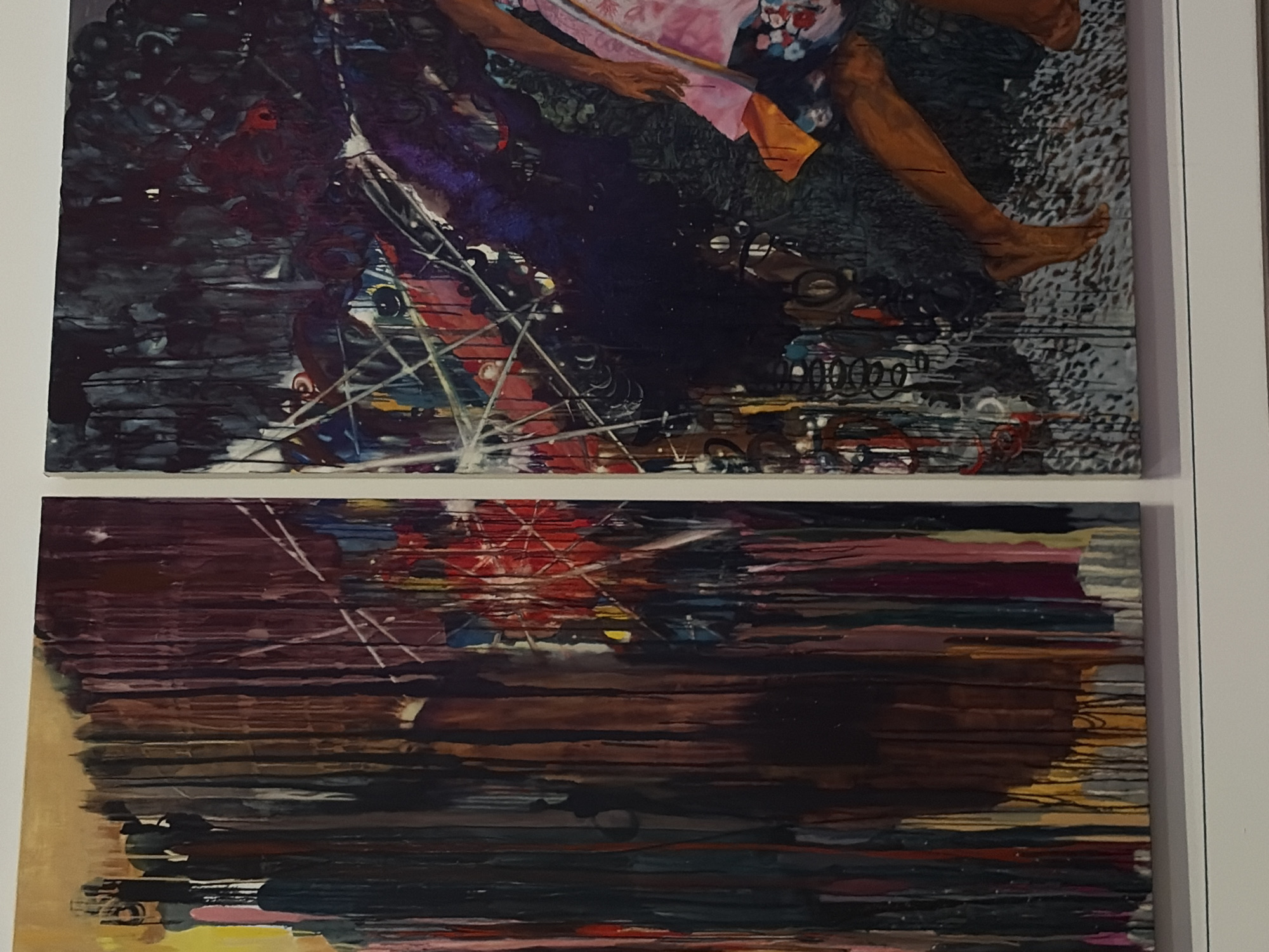 Two abstract paintings hang on a white wall. The top painting features a figure with brown skin, wearing a pink and floral garment. The figure's arms and legs are visible, along with an orange piece of fabric. The background is a mix of dark greens, purples, and grays with chaotic lines and shapes. The bottom painting is predominantly horizontal lines in shades of brown, maroon, and black, with hints of red, yellow, and blue. The location is Austin, United States of America.