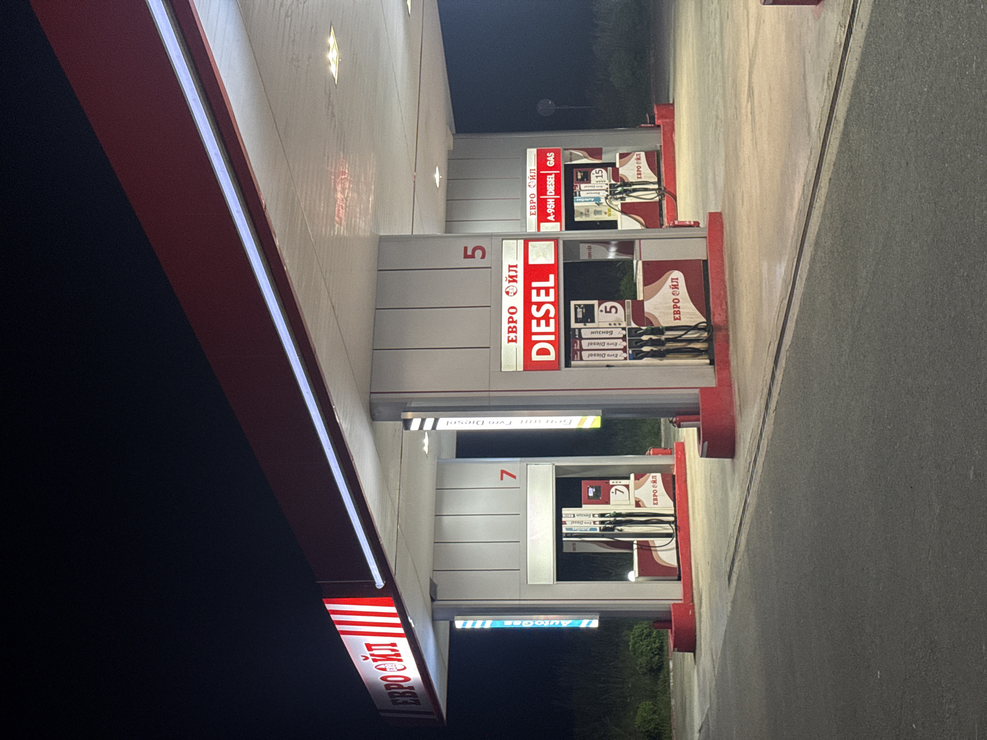 The image shows an Euro Oil gas station in Yabalchevo, Bulgaria. The station is illuminated, with signs indicating diesel fuel, A-95H, and gas availability. The pumps are numbered 5, 7 and 15. The surrounding environment appears to be at night. A paved area is next to the station.