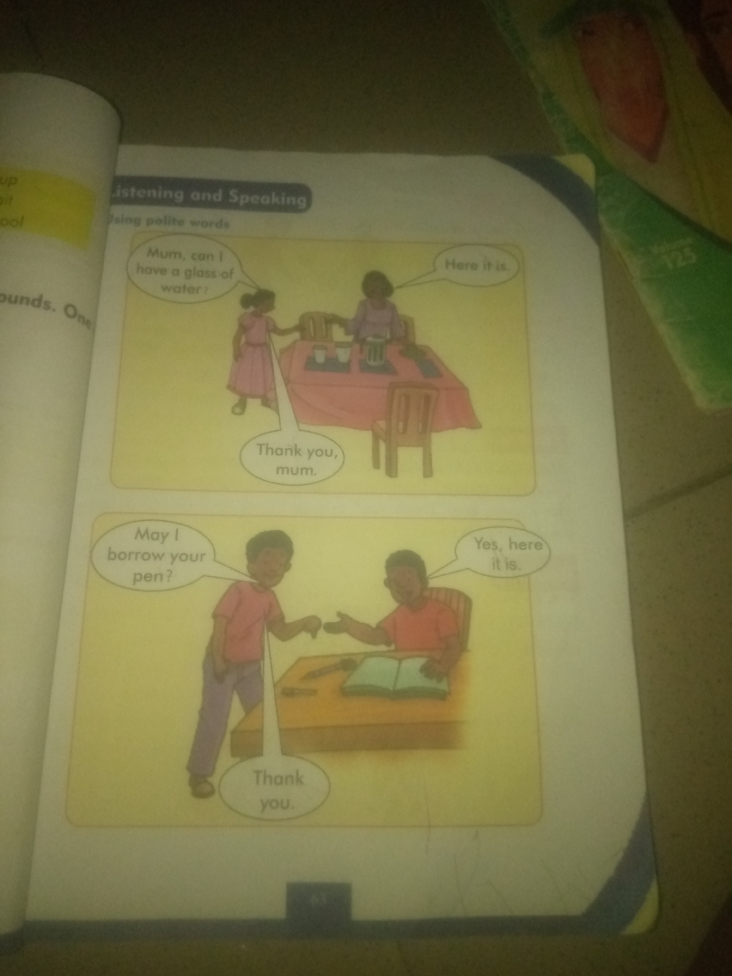 The image shows two scenes from a children's book. The top scene depicts a young girl in a pink dress asking her mother, "Mum, can I have a glass of water?" Her mother is at a table with drinks, and replies, "Here it is." The girl then says, "Thank you, mum." The bottom scene shows a boy in a red shirt asking another boy, "May I borrow your pen?" The second boy, seated at a desk with a book, replies, "Yes, here it is." The first boy then says, "Thank you." The book also contains text on the left side, with headings like "Listening and Speaking" and "Using polite words." The image is taken indoors, likely in a home or classroom setting, with a yellow border around the two illustrated scenes. There is no indication of any specific location in the city of Jauro Yinu, Nigeria.