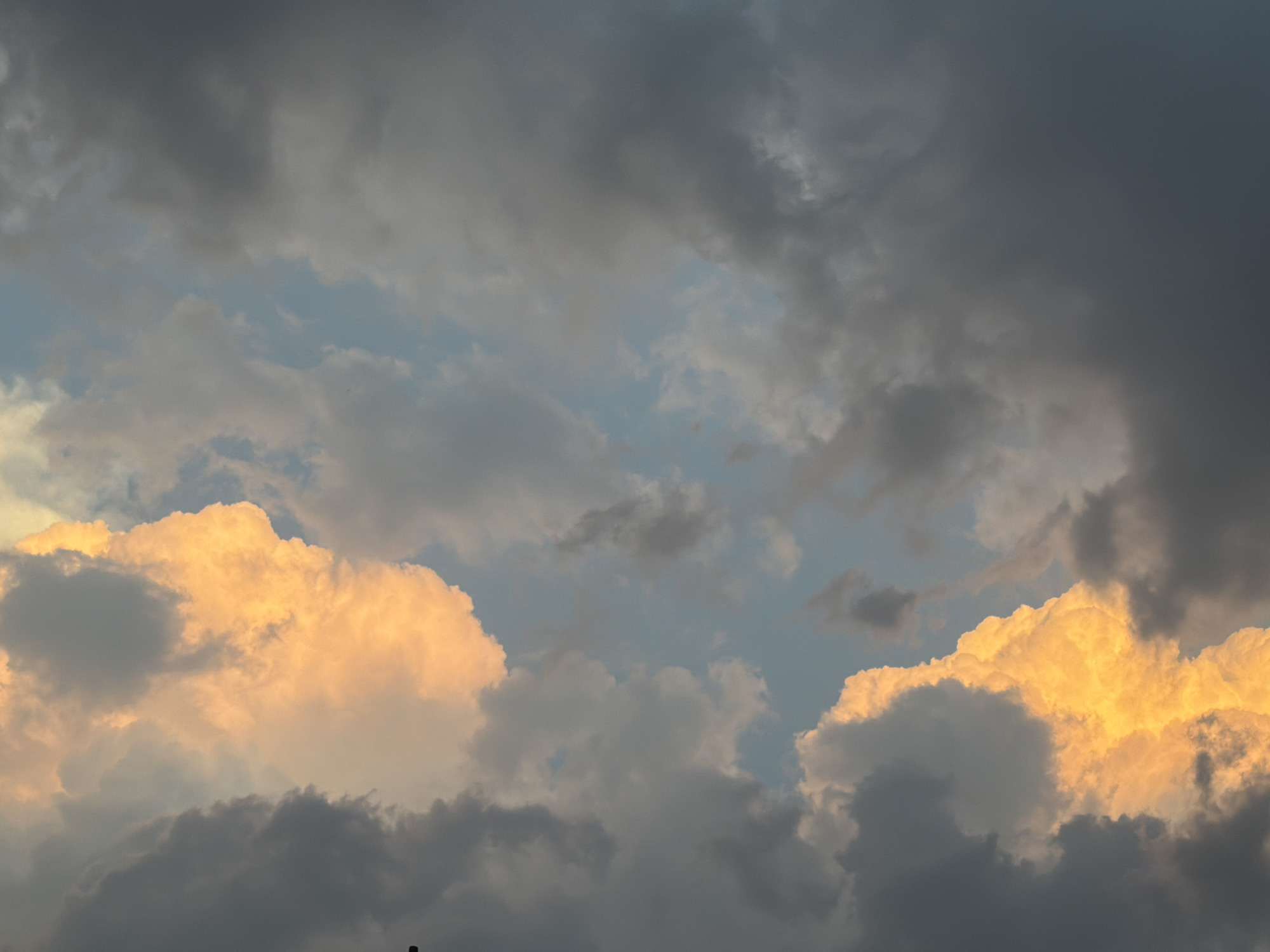 The image shows a cloudy sky. The clouds are a mix of gray and white, with some areas of light blue sky peeking through. The clouds on the bottom right and left appear golden. The image was taken in the city of Puebla, Mexico.