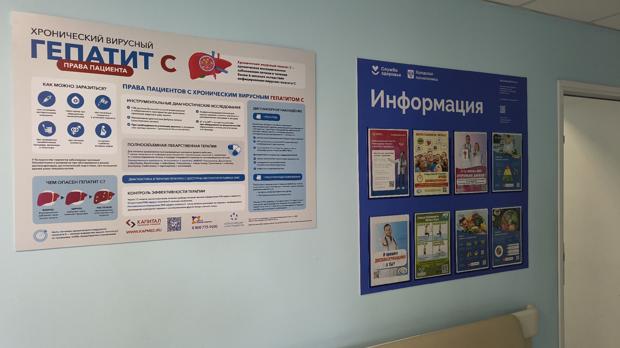 The image shows a wall in a medical facility, possibly a clinic or hospital, decorated with informational posters. On the left is a large poster titled "CHRONIC VIRAL HEPATITIS C PATIENT RIGHTS". This poster details how the infection can be contracted, diagnostic procedures, and treatment options. Below this, another poster illustrates the stages of Hepatitis C's impact on the liver.
To the right of this is a larger blue poster with the heading "Information" in prominent white lettering, under the logos of "Service of Health" and "City Polyclinic". This poster contains several smaller embedded posters with health-related messages and imagery. These include topics like "So much plan for life?", "Do you know your blood pressure?", and nutritional advice.
The wall appears to be a light color, and the posters are mounted at eye level. The overall impression is that of a public health information area within a healthcare setting. There are no people visible in the frame. The background shows a sliver of a white doorway or partition on the right.
Regarding the location of Mikhaylovka, Russia, there is no direct information within the image to confirm this specific city. However, the text on the posters is in Russian, suggesting a location within Russia. The presence of a "City Polyclinic" logo and information about the Russian healthcare system (OMS - Compulsory Medical Insurance) further supports a Russian context. Without external data or further context, pinpointing Mikhaylovka specifically is not possible from the image alone.