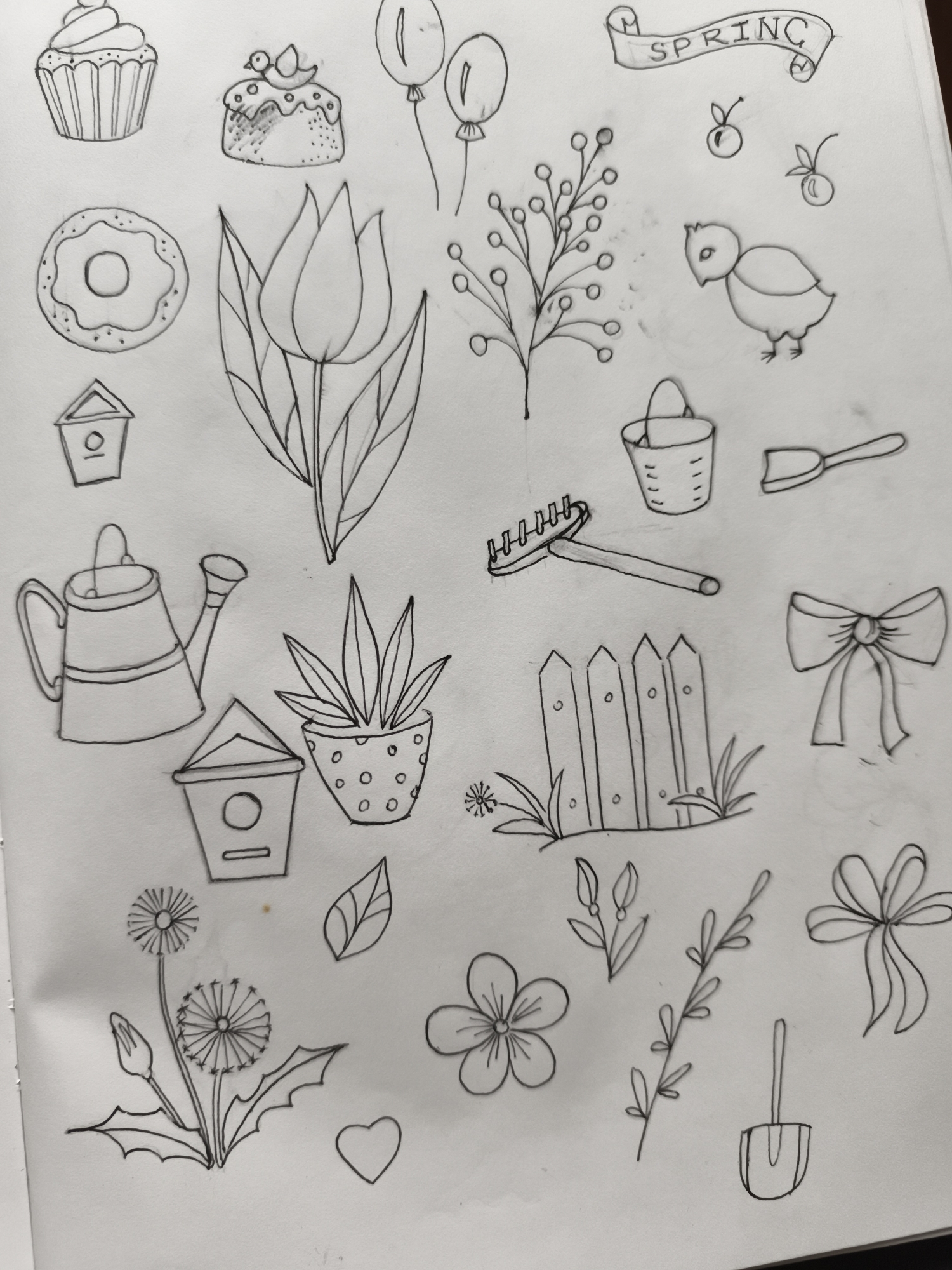 The image displays a hand-drawn illustration on a white background, featuring various spring-themed objects. The drawing is done in black ink.
The objects depicted include:
- A cupcake with frosting.
- A small cake topped with frosting and a bird.
- Two balloons.
- A banner with the word "SPRING" written on it.
- A donut.
- A tulip flower with leaves.
- A sprig of berries.
- A small chick.
- Two small red fruits with stems.
- A birdhouse.
- A watering can.
- A potted plant with spiky leaves.
- A rake.
- A bucket.
- A small shovel.
- A picket fence with grass and a small flower.
- A dandelion with a bud and a fully bloomed head.
- A single leaf.
- A small sprig with leaves.
- A single flower with five petals.
- A twig with small leaves.
- A bow.
- A heart shape.
- A small shovel.
There are no people or animals actively depicted in the drawing, only stylized representations of them. The environment is a blank white surface, suggesting the drawing is on paper. There is no indication of a specific location in Saint-Denis, France, or any city.