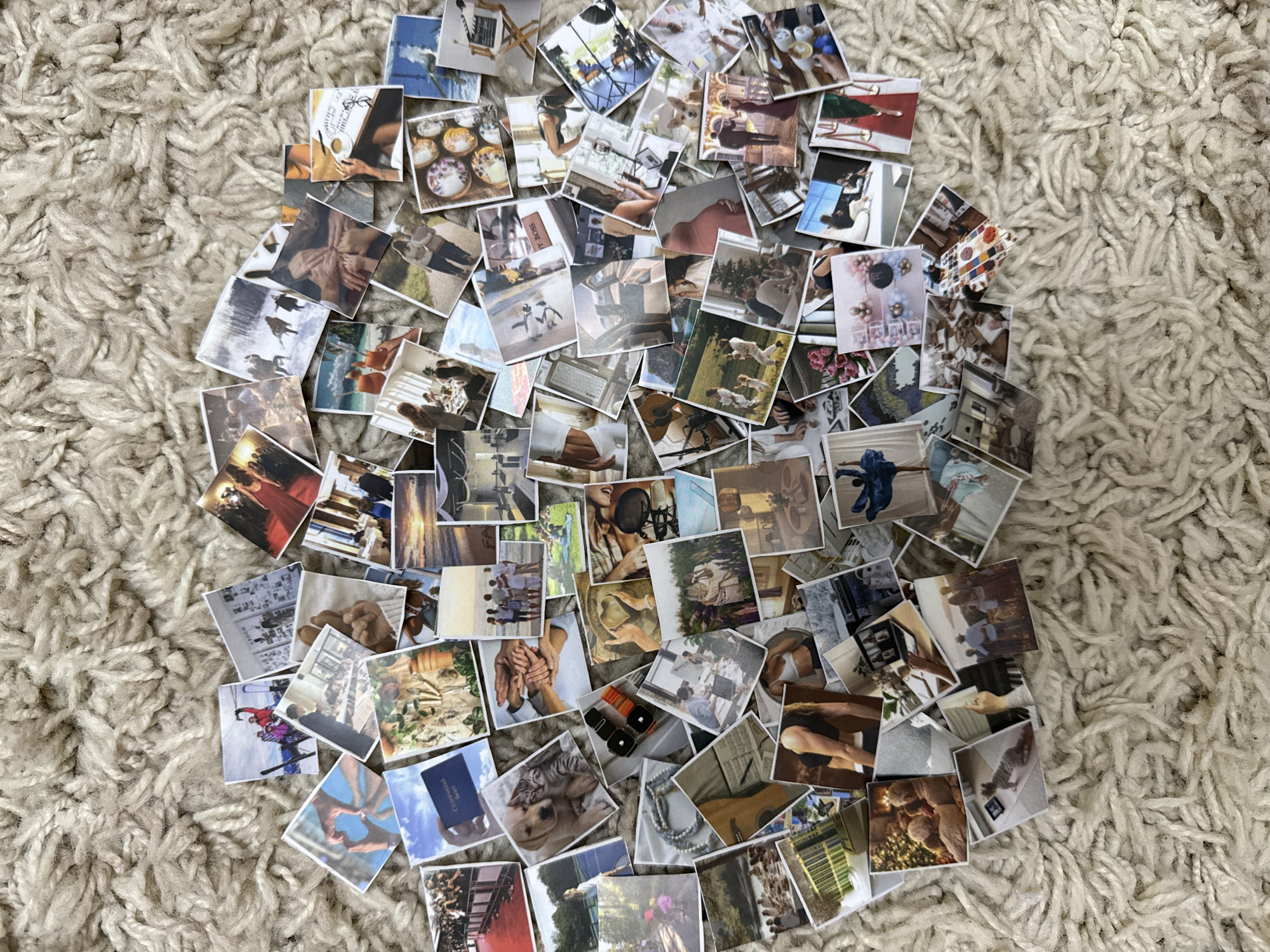 A top-down, medium shot captures a chaotic scattering of small, square photographs arranged on a textured, cream-colored carpet. The images are diverse, featuring a mix of personal memories and possibly curated content, including people in various settings such as outdoor activities, indoor gatherings, and formal events. Some photos show close-ups of objects, pets, and natural scenes. There are no recognizable landmarks or architectural elements that would indicate a specific city or location, including Khasavyurt, Russia. The carpet's texture suggests an indoor environment, likely a home or studio.