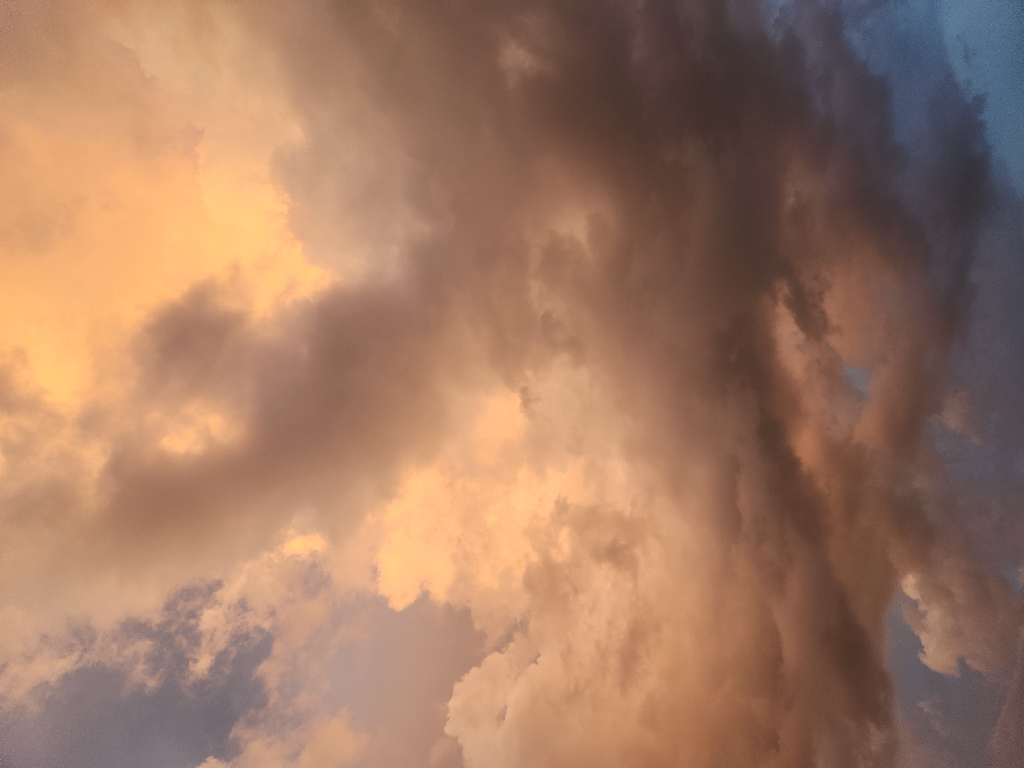 The image shows a dramatic sky filled with large, billowing clouds, predominantly in shades of orange, yellow, and gray. Some parts of the clouds are illuminated by warm, golden light, suggesting a sunset or sunrise. Other areas are darker and more ominous, with hints of blue sky peeking through in the lower portions. There are no people, structures, or identifiable landmarks in the image, only the expansive sky. The location is identified as Winter Park, United States of America.