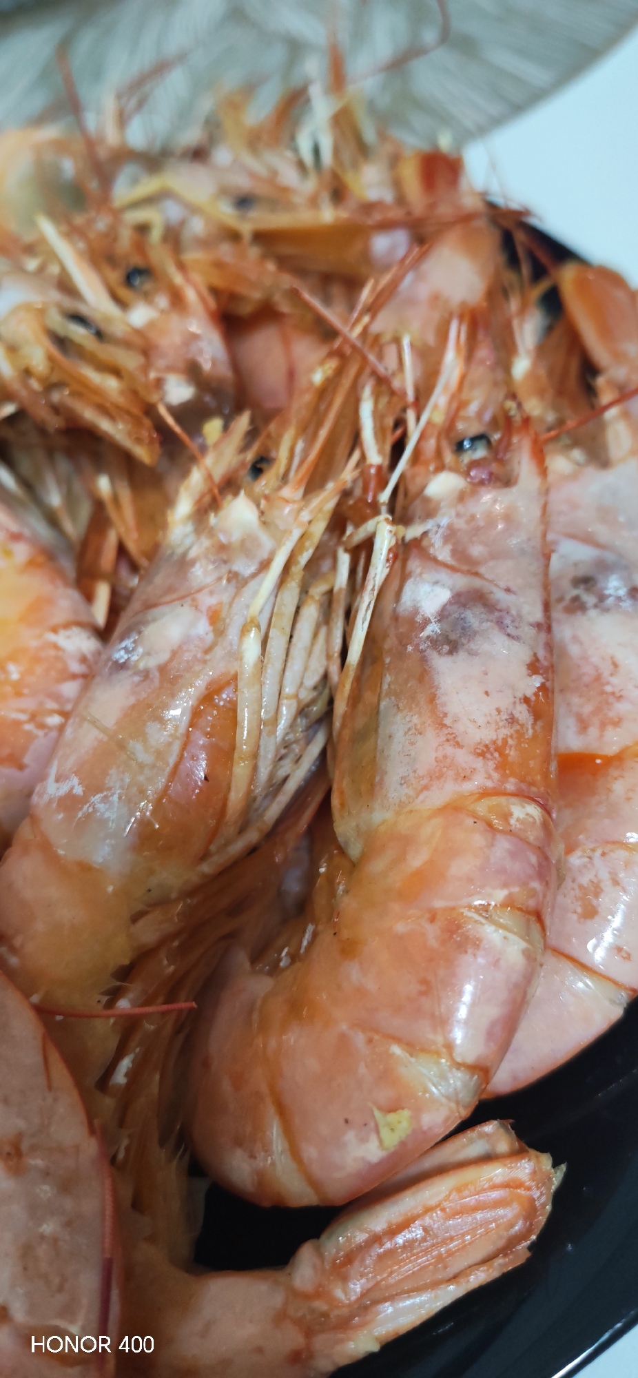 The image shows a close-up of cooked shrimp. The shrimp are orange and pink, with white antennae and legs. They are piled on top of each other. There is a logo for HONOR 400 at the bottom left of the image. There is no indication that this is Noviy, Russia.