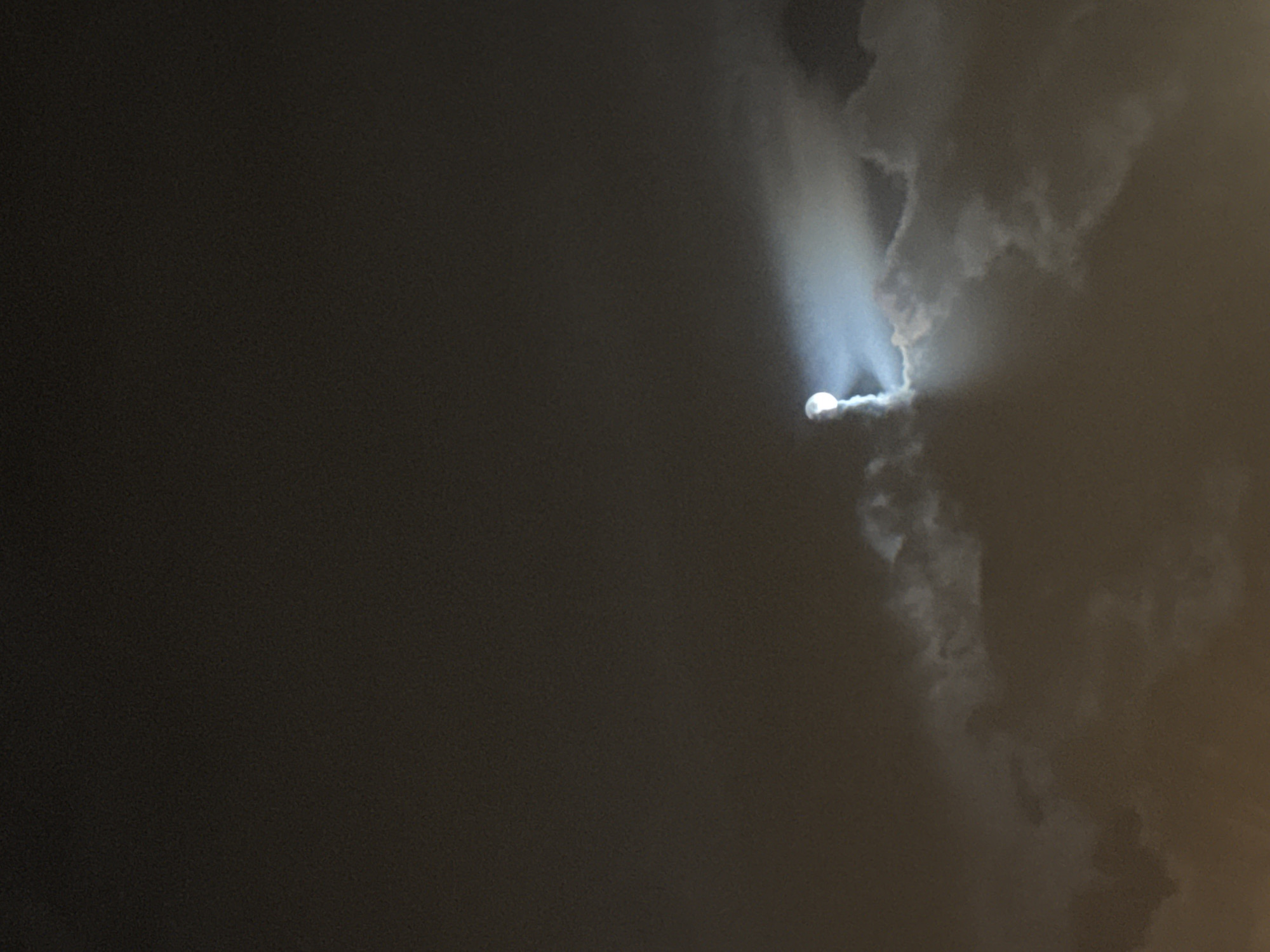 A photograph taken at night depicts a bright, circular object surrounded by luminous trails against a backdrop of dark clouds. The object is emitting a bright light, and the trails appear to be emanating from it. The surrounding clouds are a mix of gray and white tones, with the brighter clouds concentrated near the light source. A significant portion of the image is dark, suggesting that it was taken during nighttime or in dim lighting conditions. There is no indication of the location being Moscow, Russia, or any people present in the image.