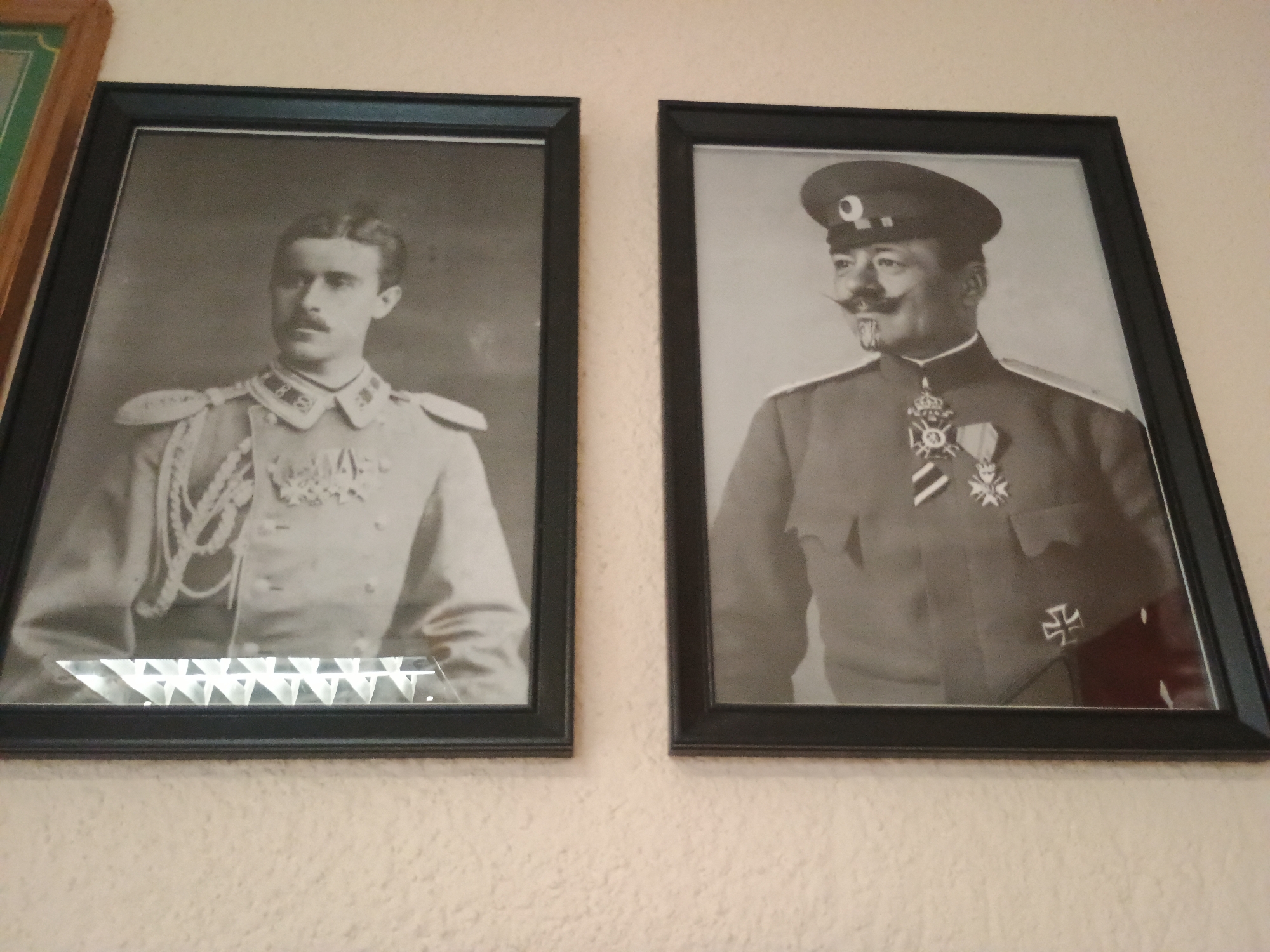 The image depicts two black and white portraits in dark frames hanging on a light-colored wall. The portrait on the left shows a man in a military uniform with medals and a mustache. The portrait on the right shows another man in a military uniform and hat, also with medals and a distinctive mustache.
While the image itself does not inherently reveal location details, the context of being in Plovdiv, Bulgaria, suggests these portraits are likely of Bulgarian military figures or historical figures significant to Bulgarian history.
