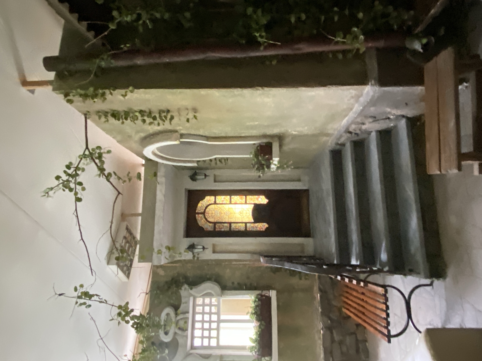 This photograph appears to be taken from an unusual, tilted perspective, capturing an outdoor scene that could be part of a building's exterior. The main focal point is a doorway with a distinctive decorative window, suggestive of an older architectural style. A set of stairs leads up to the doorway on one side.
The surrounding environment is embellished with greenery, including climbing plants covering parts of the walls. A window with a detailed frame is also visible, further adding to the architectural details of the building. A bench is positioned to the side of the stairs, possibly offering a place to sit and enjoy the surroundings.
It is hard to confirm the exact location in Yekaterinburg, Russia.
