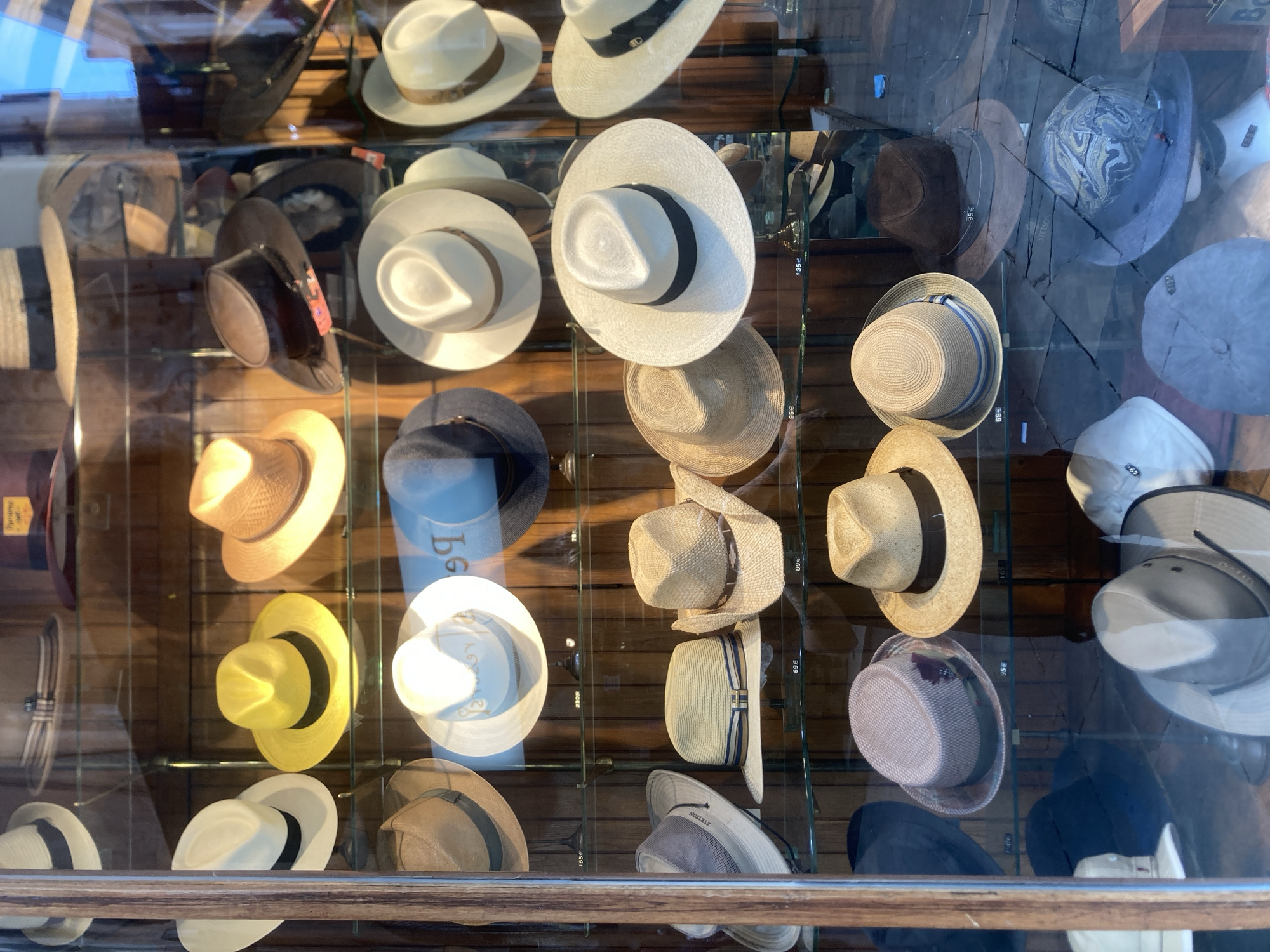 The image depicts a display window of a hat shop. The window is filled with a variety of hats, arranged on multiple shelves. The hats are of different styles, colors, and materials, including straw hats, fedoras, and possibly some more casual caps. The display is well-lit, and the hats are presented in an orderly fashion. The background appears to be a wooden wall, common in retail settings. There is a price tag visible on some of the hats, indicating they are for sale. The overall impression is of a well-stocked and organized hat boutique.
Based on the information available, the hat shop is located in Barcelona, Spain.