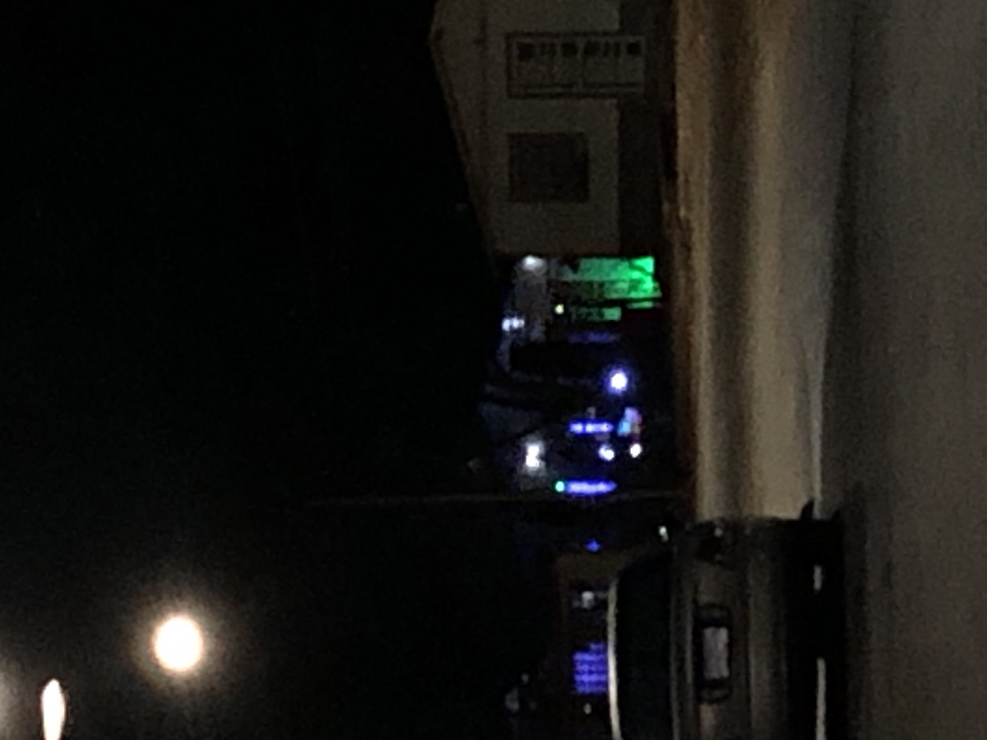 The image shows a nighttime scene in Altagracia, Venezuela. A dark sky occupies the left side of the frame. A building with lit windows and a sign is positioned near the top-center. Down below is what appears to be dashboard of a vehicle. Finally, a vertical wall with a rough texture takes up the right side of the image. There are no people visible. The scene appears to be captured from inside a car or vehicle.