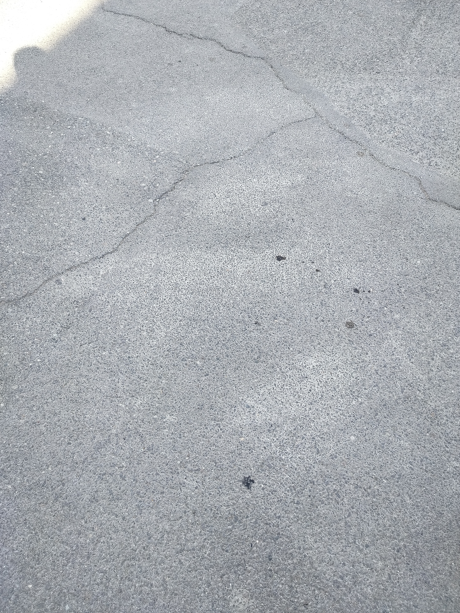 The image depicts a section of cracked asphalt pavement. The texture is coarse and speckled, typical of asphalt. Cracks run across the surface. The photo appears to have been taken during the day. The location is unknown but it is supposedly in Yerevan, Armenia. No people, subjects, objects, actions, or interactions are directly visible in the scene beyond the cracked asphalt surface.