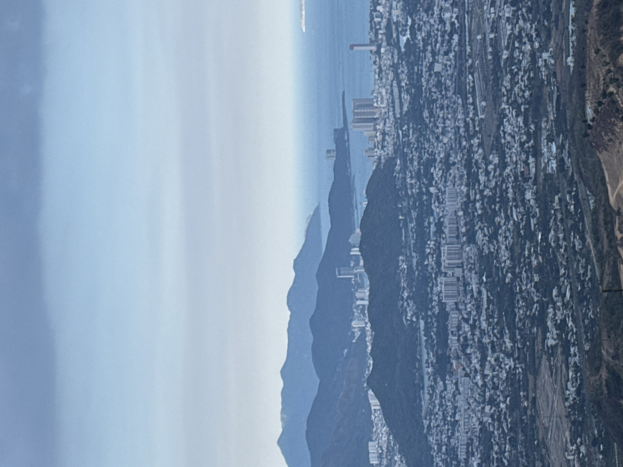 The image shows a coastal city, with a large number of buildings, next to a series of mountain ridges, under a pale blue sky. The buildings appear densely packed. The location seems unlikely to be Diên Khánh, Vietnam, as Diên Khánh is inland. The coastal city may be the result of incorrect labeling.