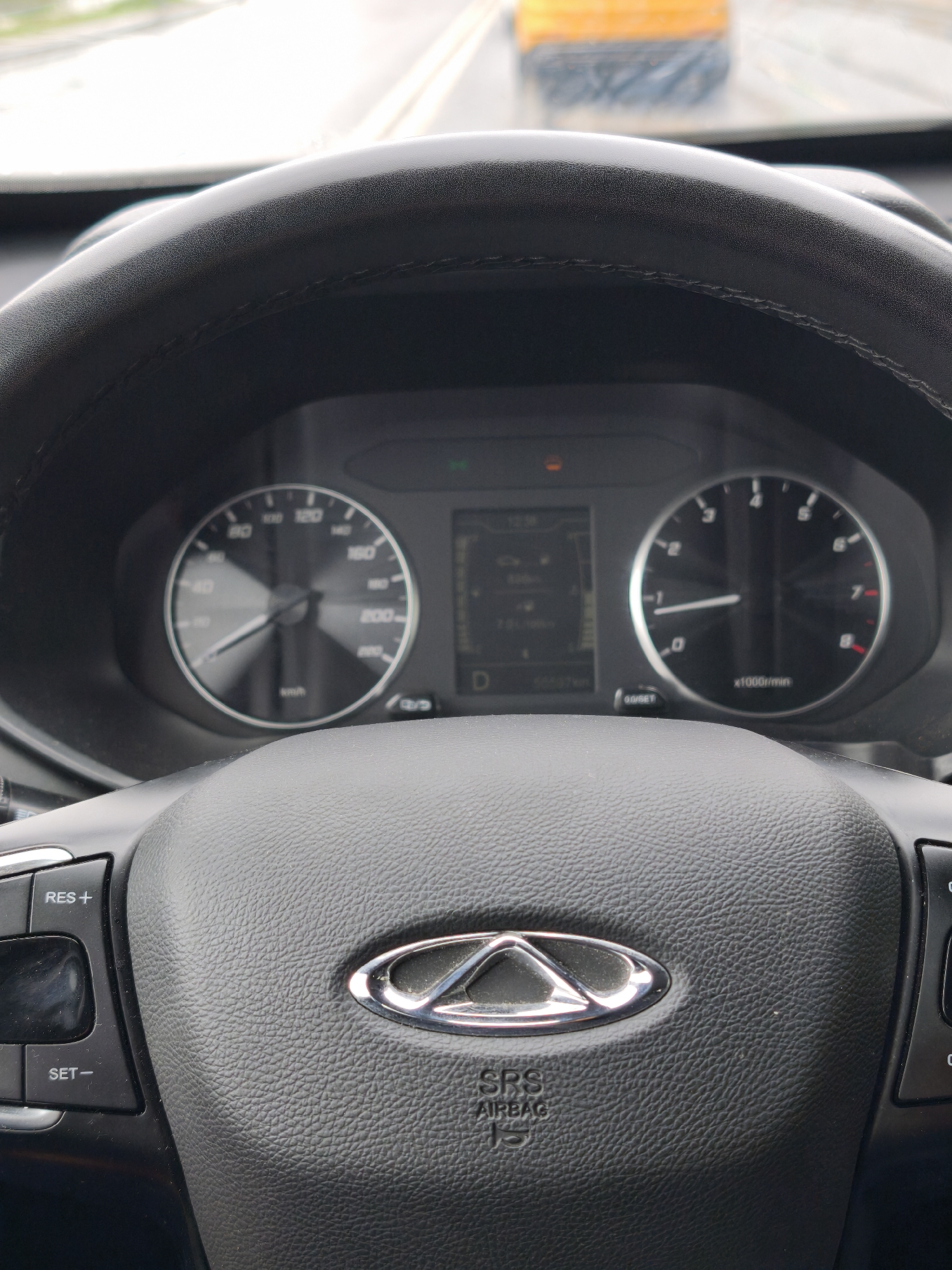 The image depicts the interior of a car, focusing on the steering wheel and dashboard. The steering wheel is black, with the car's logo prominently displayed in the center. The dashboard features a speedometer, a tachometer, and a digital display showing various vehicle information. The car appears to be in motion, with an indistinct object visible through the windshield. There is no evidence in the image to determine if it is in the city of Moscow, Russia.