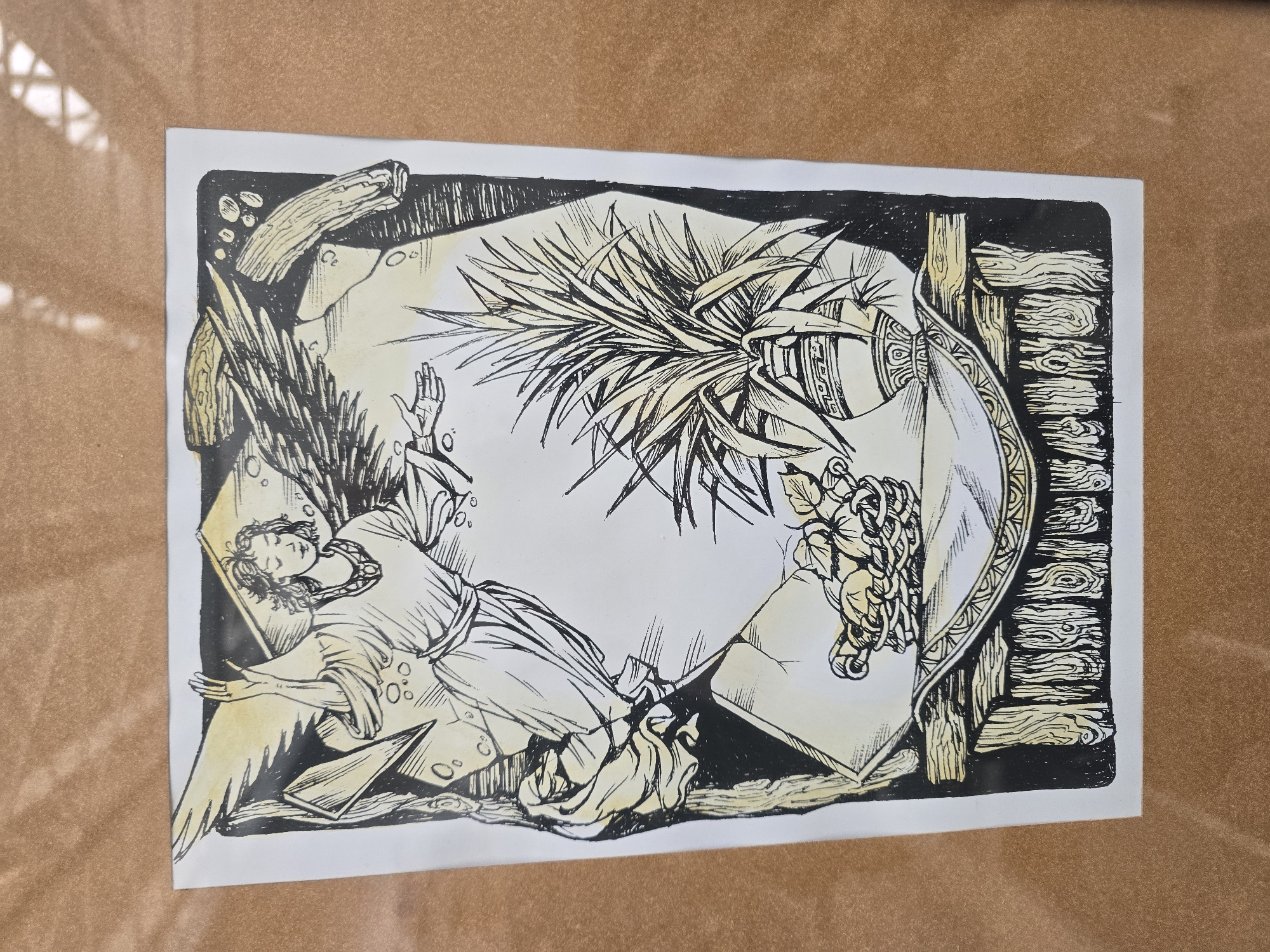 The image shows a drawing featuring an angel lying with outstretched arms, next to a pineapple plant and grapes. The composition is framed within a rough-hewn wooden border. The drawing is in black and white with yellow highlights. The location is unknown.