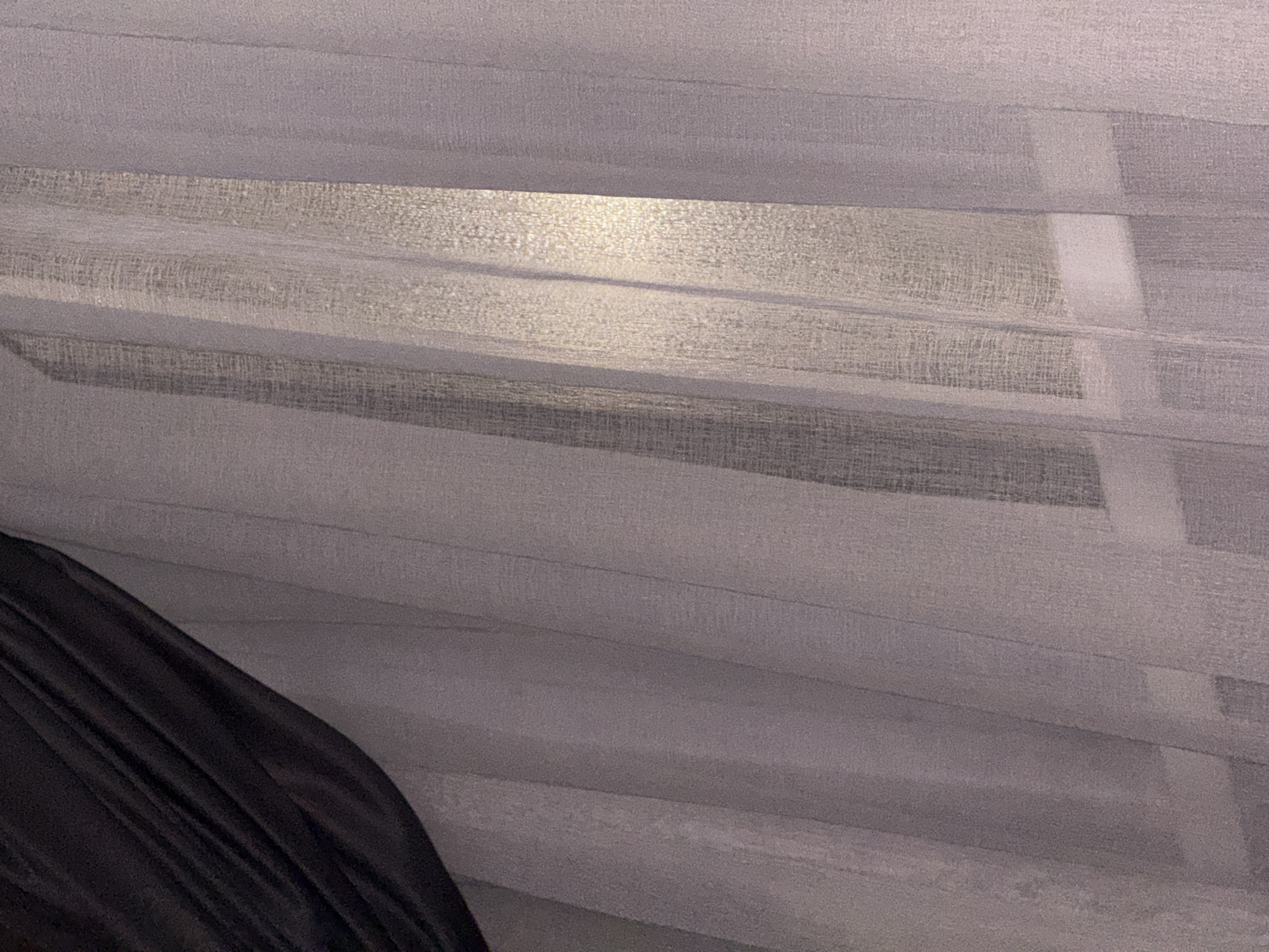 The image depicts a close-up view of sheer curtains, partially obscured by a dark, draped fabric on the left side. The sheer curtains are a pale, translucent material, exhibiting vertical folds and a subtle texture. Light filters through the fabric, creating areas of brightness and shadow, particularly a prominent vertical band of illumination in the center right of the frame. The setting appears to be indoors, suggesting a window with curtains. The image lacks any discernible human presence, identifiable landmarks, or specific environmental cues that would allow for the determination of a location within Doma 1096 Km, Russia.