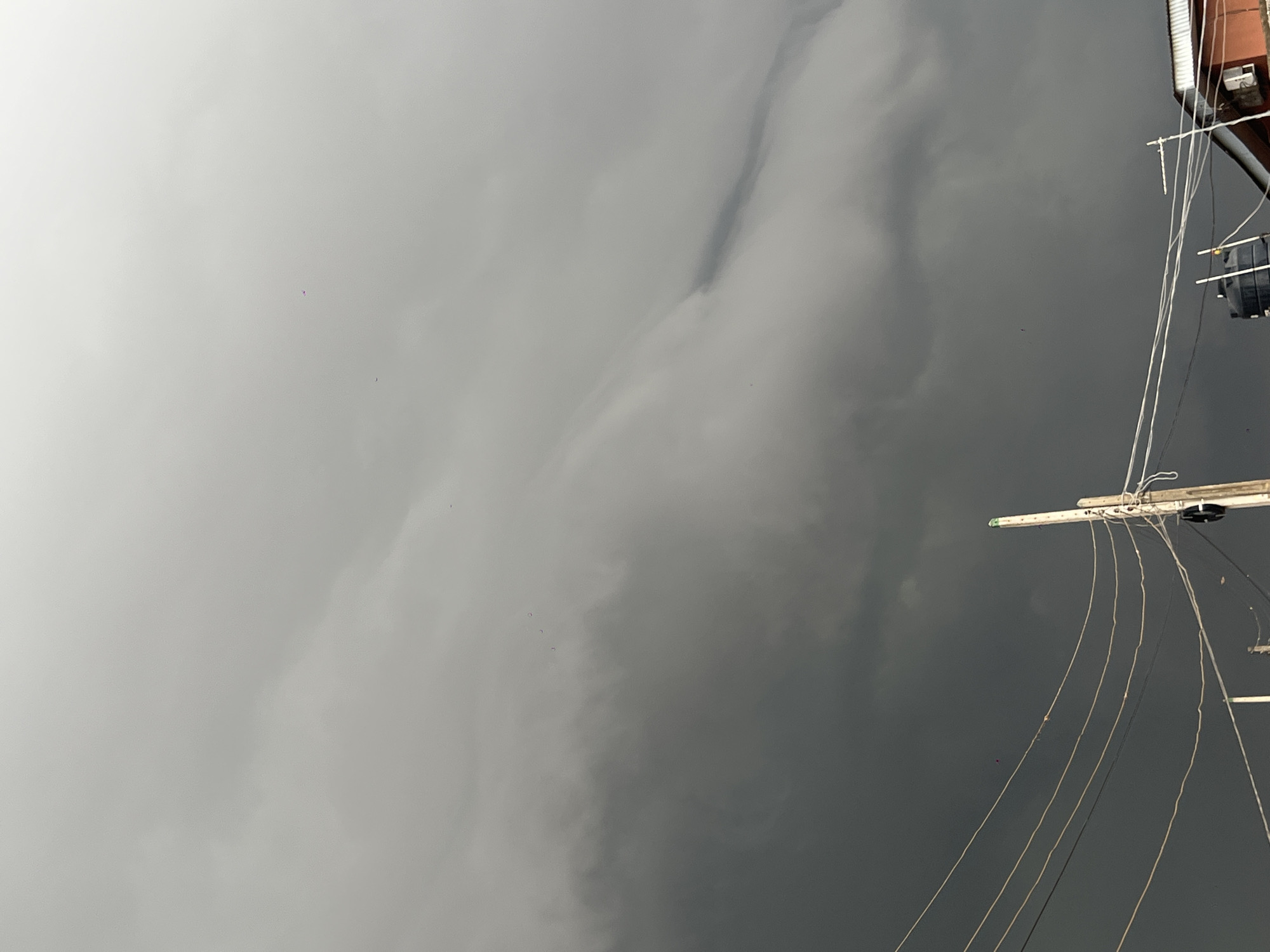 The image depicts a cloudy sky, ranging from light gray to dark gray, with a few scattered pink objects. The corner of a structure with wires is visible in the top right of the frame. The location is Egan, Nigeria, but there is no other information about the location in the image. There are no people, subjects, objects, actions, or interactions beyond what has been described.