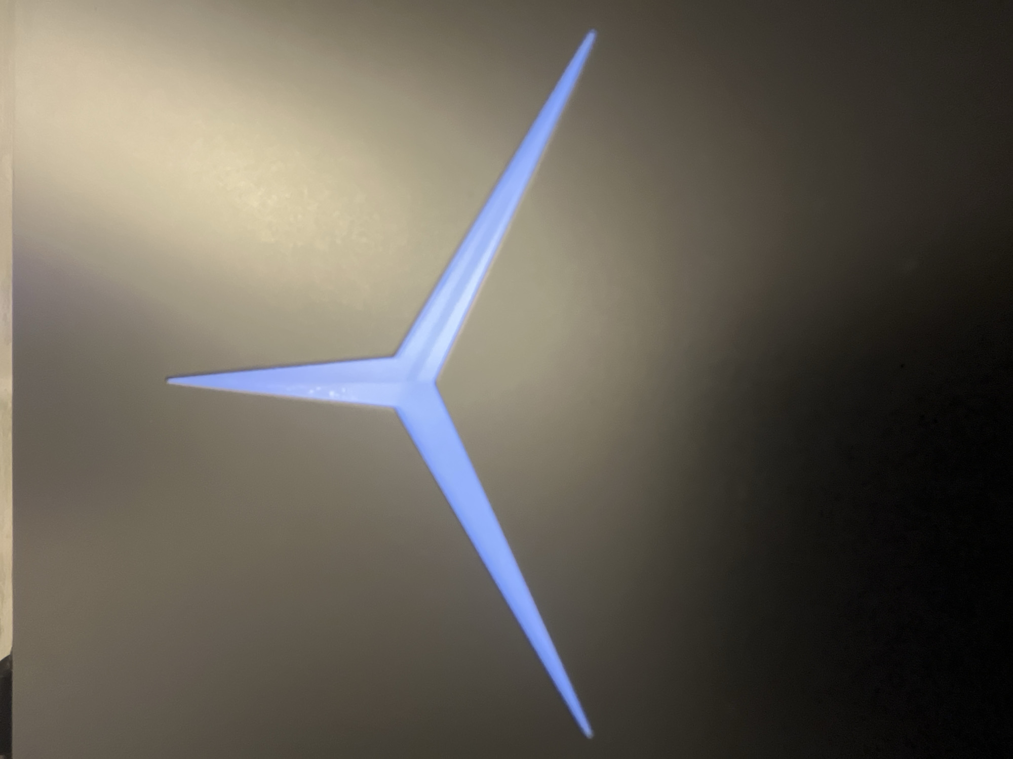 A close-up image of a Lenovo Legion logo, illuminated in a light blue hue, against a dark gray or black background. The logo is centrally positioned and takes up a significant portion of the frame. The background has areas of light reflection or unevenness.