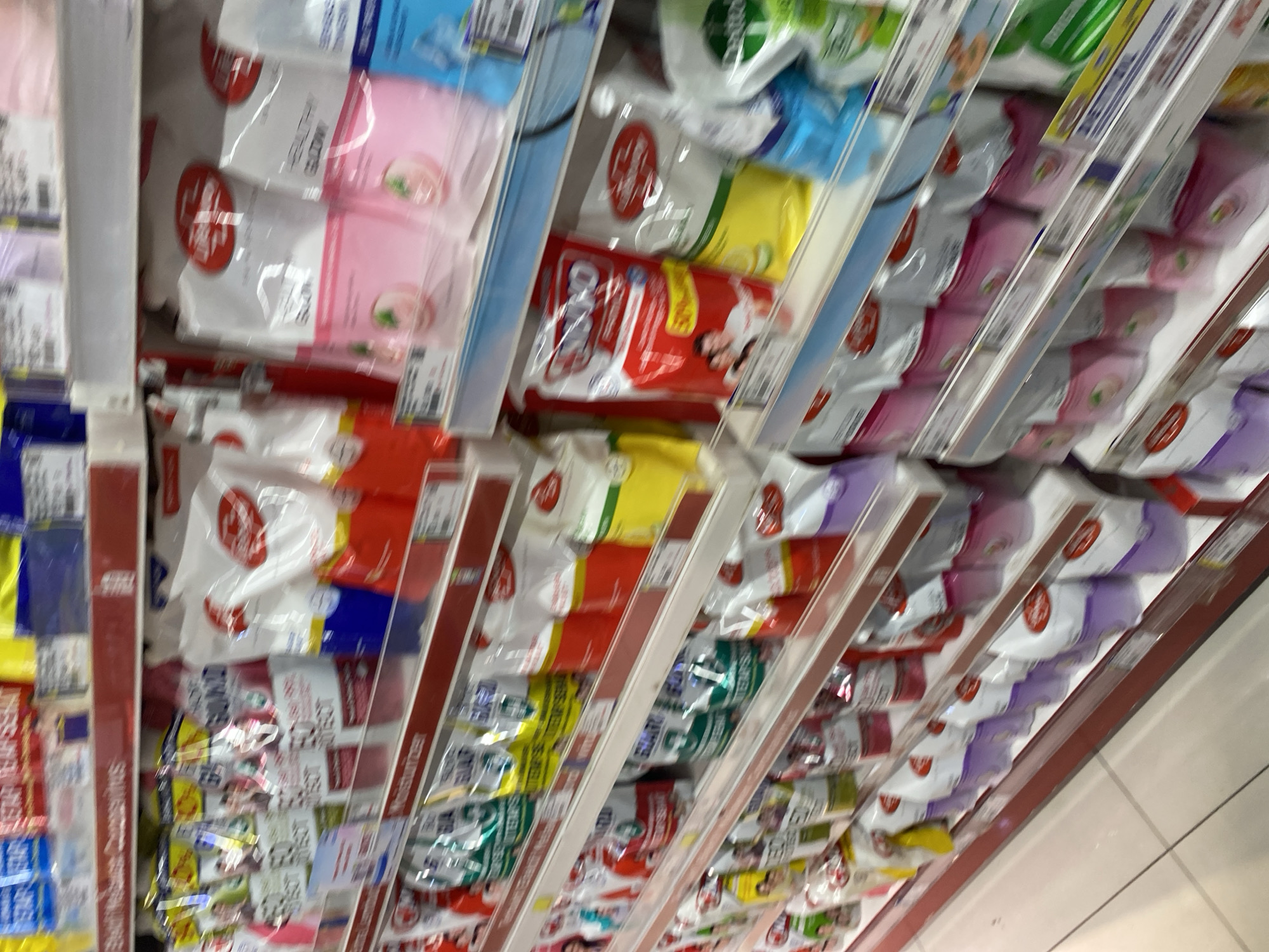 The image shows shelves of various personal care products, likely in a supermarket or convenience store in Banda Aceh, Indonesia. The products are primarily pouches of liquid soap, shampoo, or body wash, displayed in multiple rows on white shelves. The packaging features a variety of colors, including red, green, yellow, blue, pink, and white, with some showing images of people or fruit. The lighting appears to be artificial, typical of an indoor retail environment. The overall impression is a well-stocked retail display.