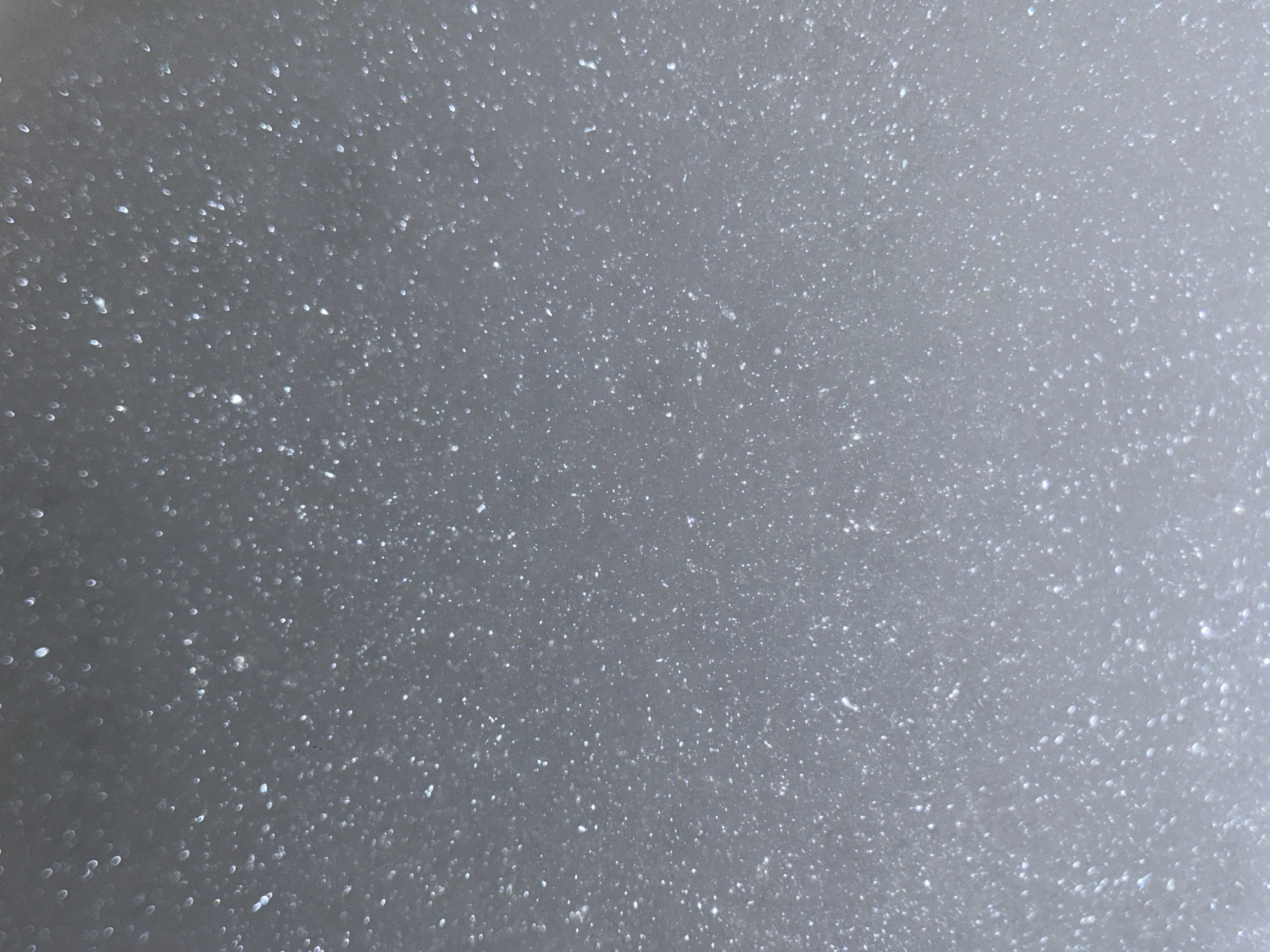 The image shows a close-up view of snowflakes on a surface. The snowflakes appear as small, bright, blurry spots scattered across a gray background. There are no people or specific objects visible. The focus is solely on the texture and pattern of the snowflakes. The image does not contain any discernible details relating to the city of Moscow, Russia.