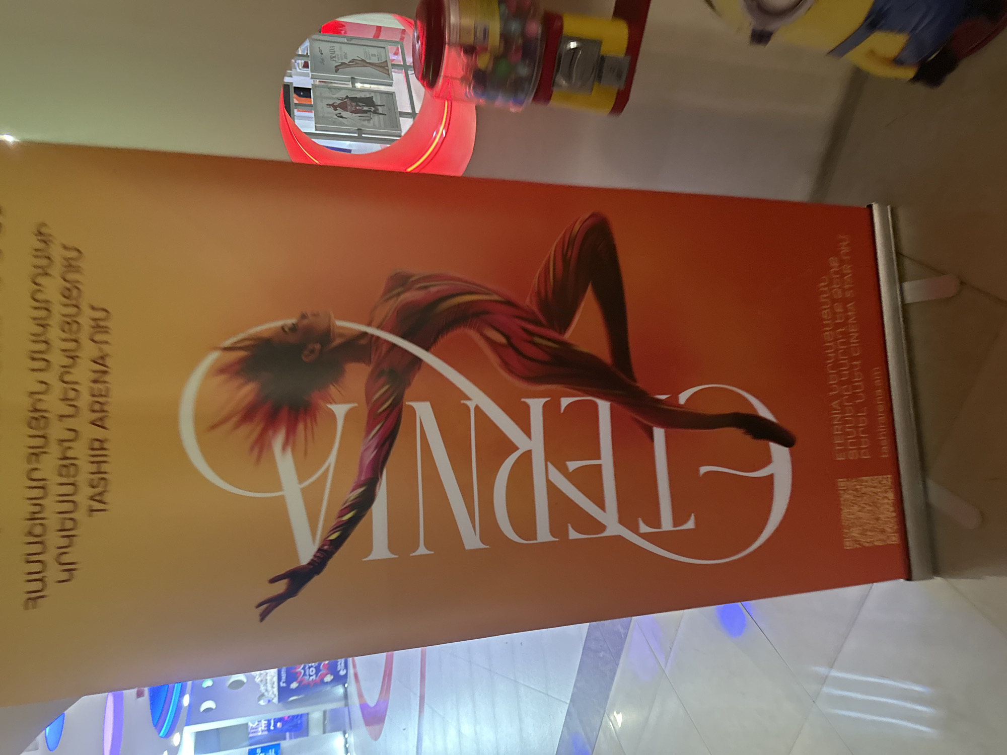 The image shows a promotional banner for "Eternia," a circus performance taking place at Tashir Arena in Yerevan, Armenia. The banner features a stylized image of a performer in a contorted pose, with the word "Eternia" prominently displayed. Additional text in Armenian is visible. The banner is positioned indoors, likely within or near the venue.
