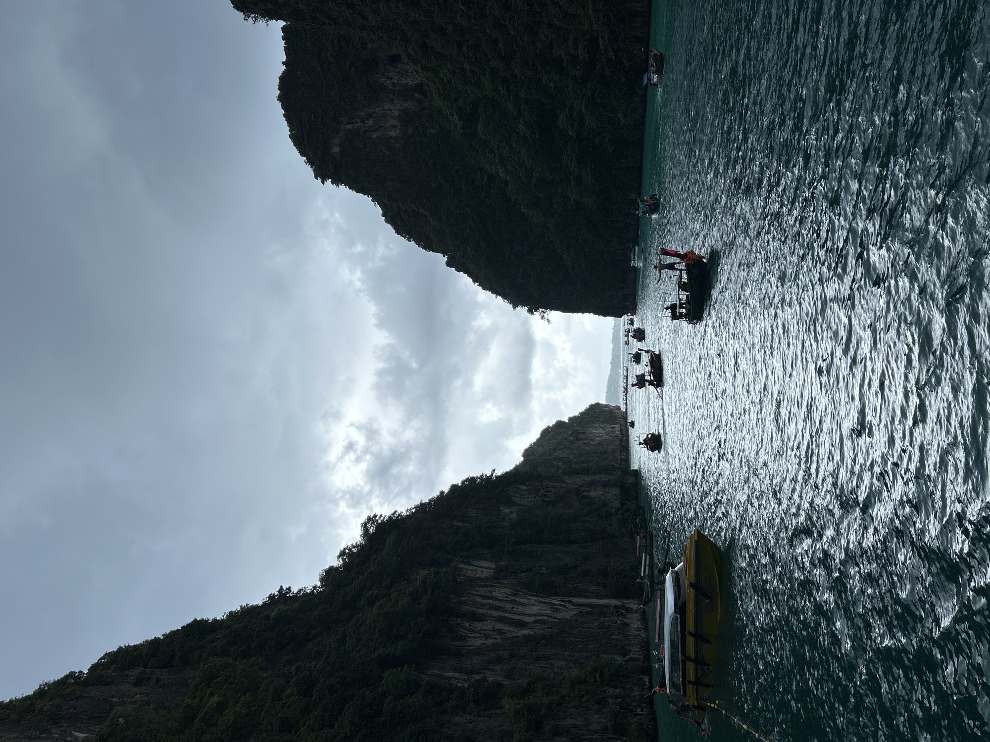 The image depicts a body of water surrounded by sheer, verdant cliffs under a cloudy sky. Several longtail boats, some with people visible, are scattered across the turquoise water. The scene appears to be a scenic bay or channel. The question asks about the location in Haad Yao, Thailand. This image appears to be a classic view of the Phi Phi Islands, Thailand, which is a popular tourist destination known for its dramatic limestone cliffs and clear waters. Haad Yao is a beach on Koh Phangan, a different island in Thailand. Therefore, the image is not of Haad Yao, Thailand.