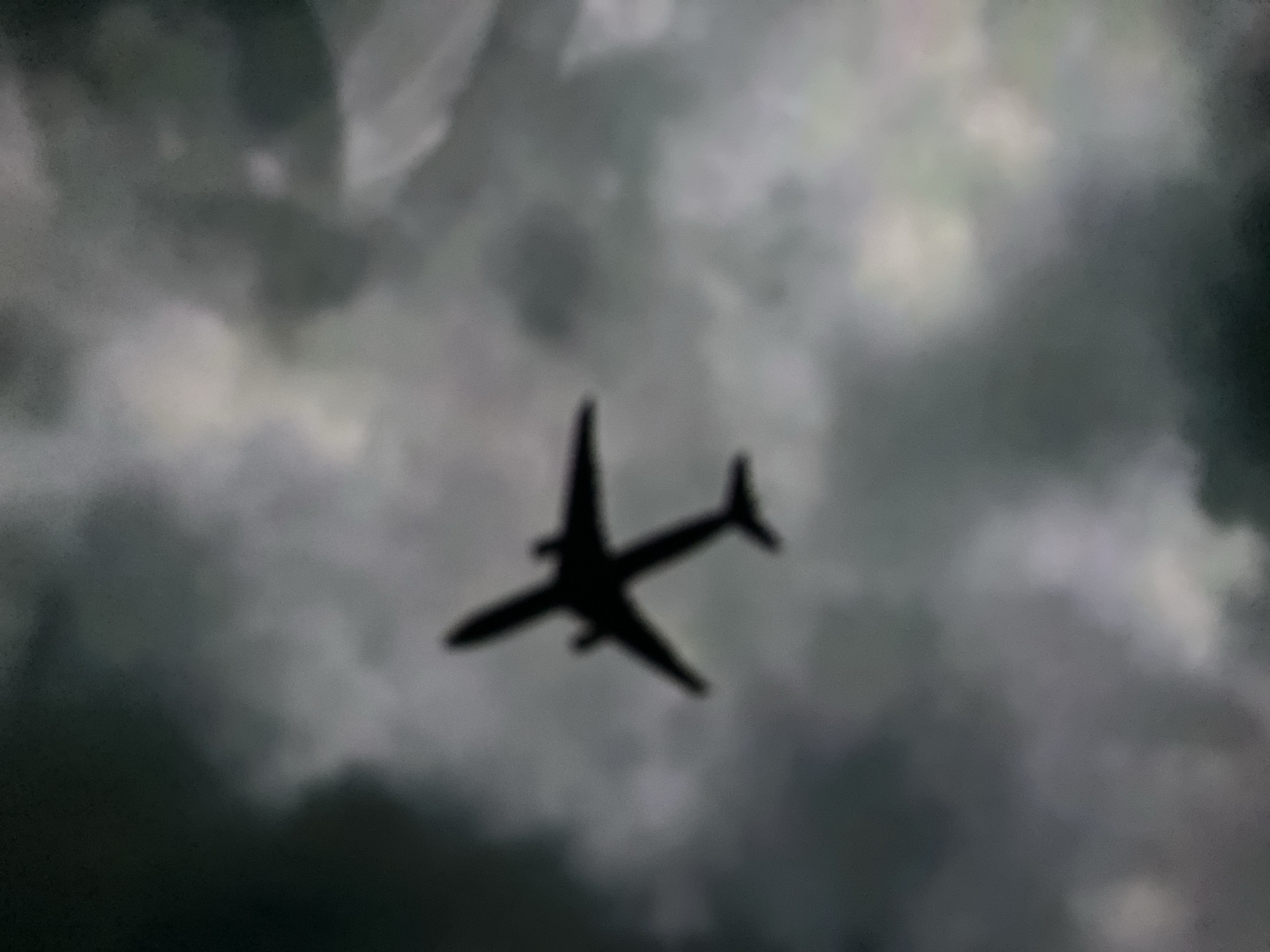 The image shows a silhouetted airplane against a cloudy sky. The airplane is in the center of the frame, with its wings extended. The sky is filled with dark, turbulent clouds, suggesting stormy weather. There is no discernible location in the city of Aktobe, Kazakhstan, or any specific details about people, objects, actions, or interactions.