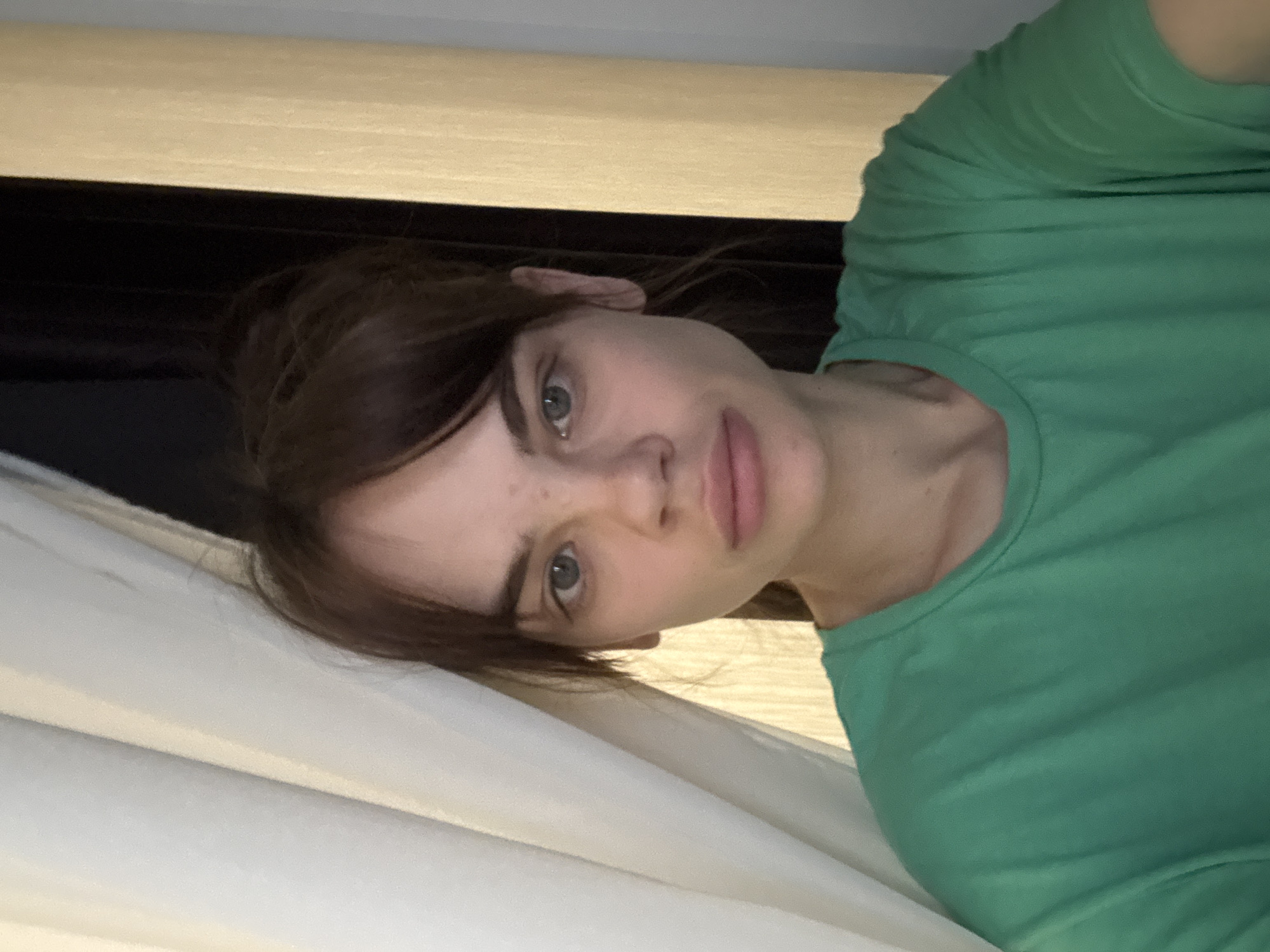 A person with brown hair and blue eyes is wearing a green shirt. The background includes a white curtain, a dark horizontal band, and a light-colored surface. There is no information to identify the location as Rostov-on-Don, Russia.