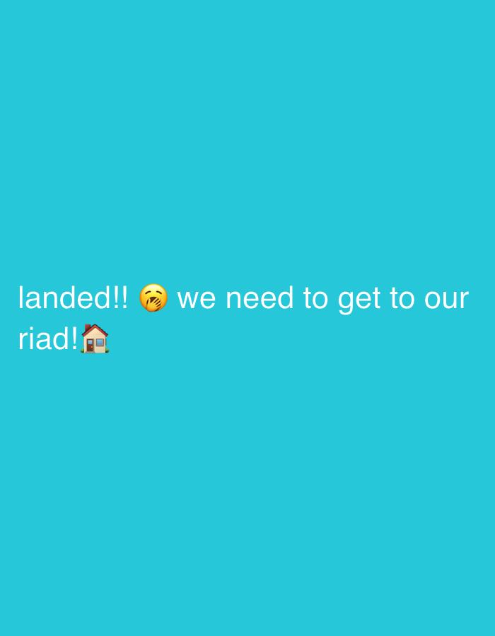 The image displays white text on a bright turquoise background. The text reads, "landed!! 😱 we need to get to our riad! 🏡". The first line of text is "landed!!". To the right of this is a face with tears of joy emoji, followed by "we need to get to our". The second line of text is "riad! 🏡", with a small house emoji to the right of "riad!". The riad, a traditional Moroccan house with an interior courtyard or garden, is a common form of accommodation in Marrakech.