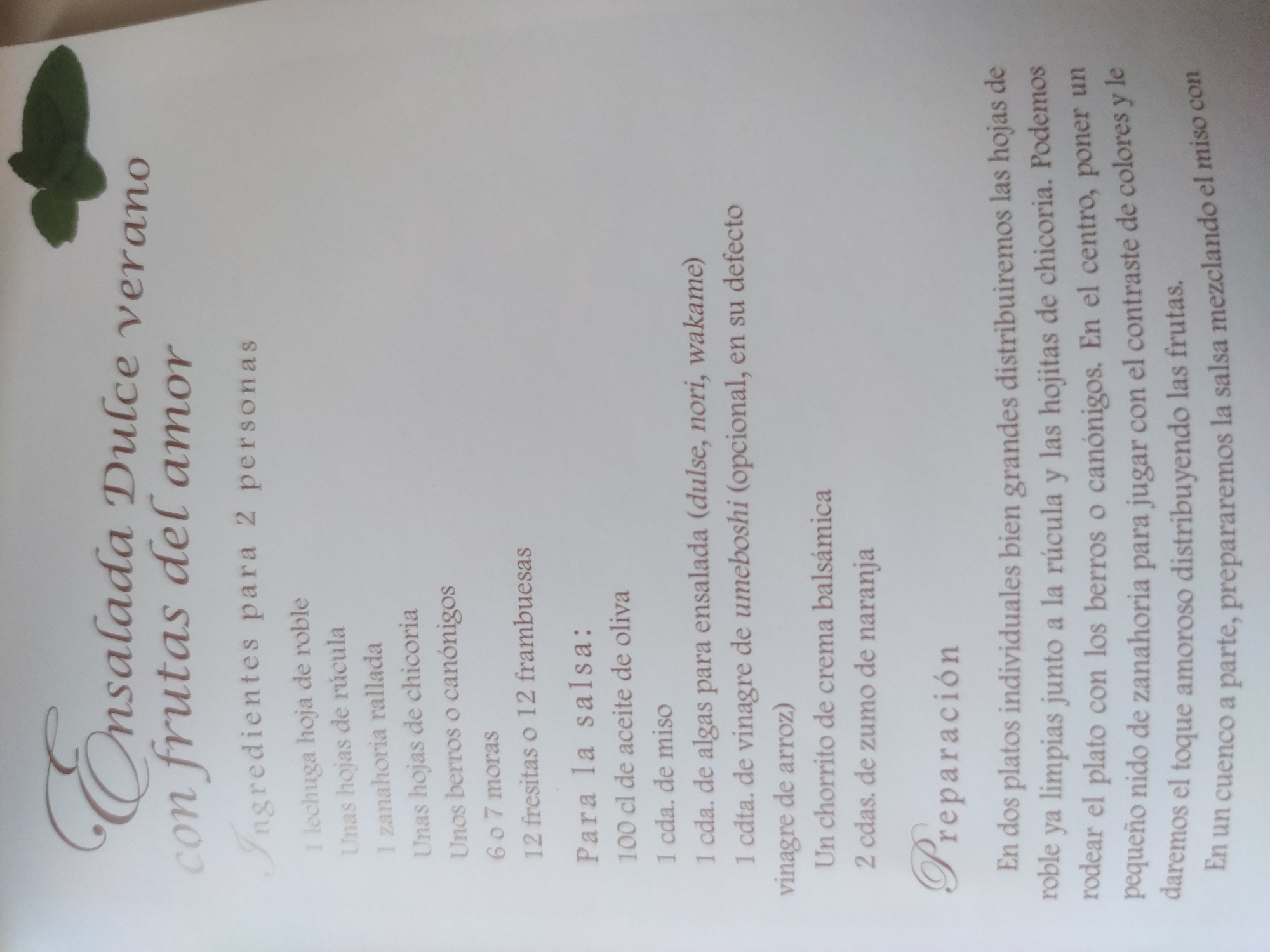 The image is a close-up of a page from a recipe book, likely printed on textured paper. The recipe is titled "Ensalada Dulce verano con frutas del amor," which translates to "Sweet Summer Salad with Fruits of Love." The text is in Spanish.
The page lists ingredients for two people, including oak leaf lettuce, arugula, grated carrot, chicory leaves, watercress or lamb's lettuce, blackberries, strawberries or raspberries, olive oil, miso, salad algae (dulse, nori, wakame), umeboshi vinegar (or rice vinegar), balsamic cream, and orange juice.
The preparation section describes arranging the lettuce, arugula, and chicory leaves in large individual plates. Watercress or lamb's lettuce can be used to surround the plate, and a small "nest" of carrots is placed in the center. Fruits are distributed to create a contrast of colors. The sauce is prepared separately by mixing the miso.