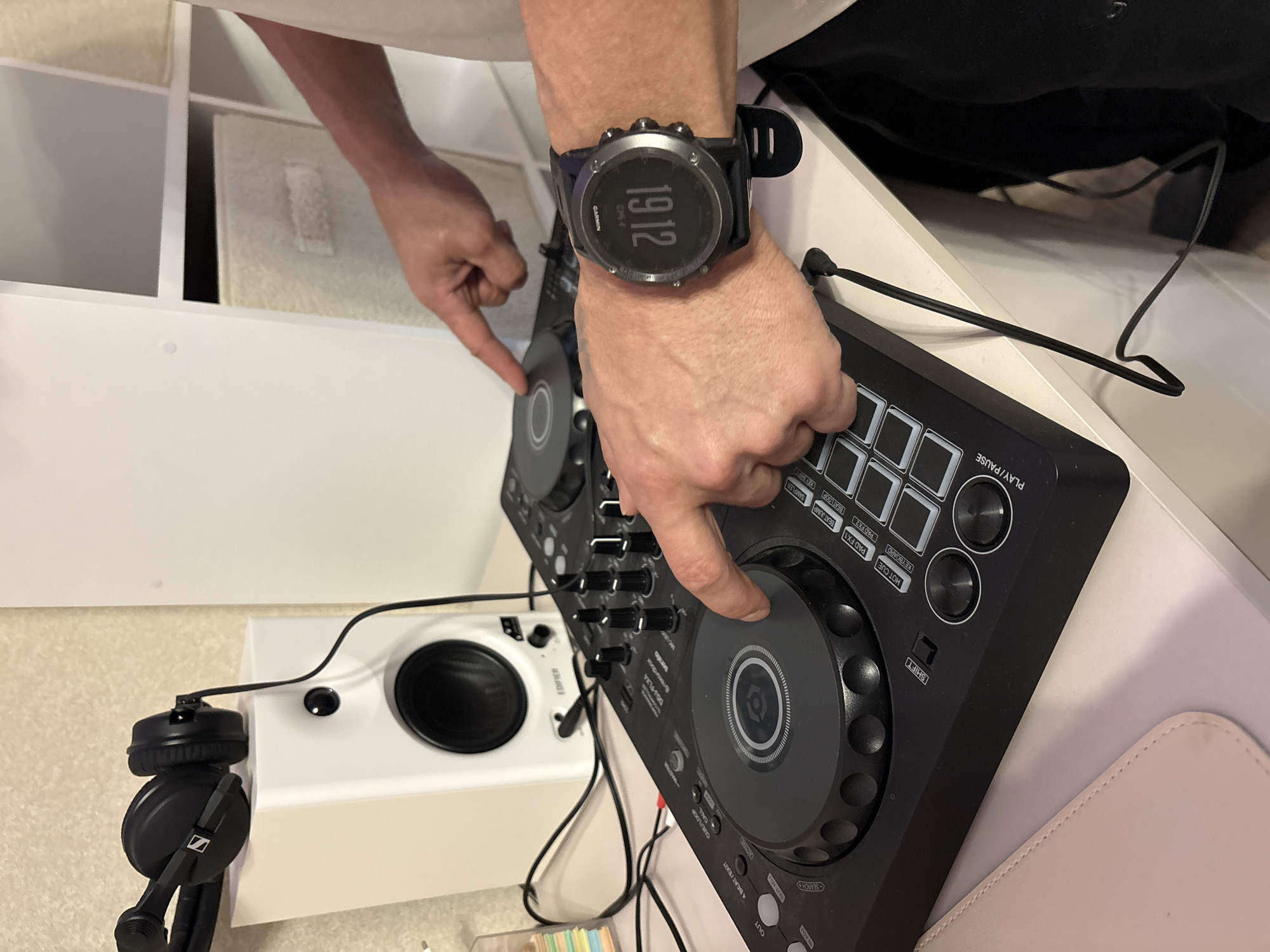 A person wearing a Garmin watch with the time 19:12 is interacting with a Pioneer DJ DDJ-FLX4 DJ controller. The person's fingers are touching the jog wheels of the controller. Next to the controller is an Edifier speaker and a pair of Sennheiser headphones. The scene is set indoors, possibly in a studio or home environment. The location in the city of Кондратово, Russia, is not discernible from the image.
