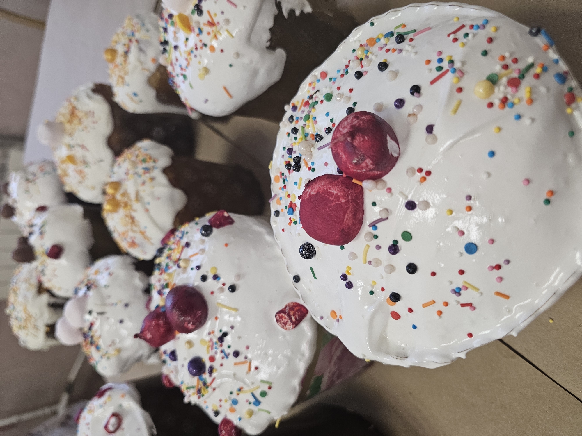 The image shows several Easter cakes, known as kulich, in a cardboard box. The cakes have a cylindrical shape and are covered with white icing, decorated with colorful sprinkles and red candied fruits. The background is a neutral brown color, likely the inside of the box.
While the image does not explicitly state that the location is Moscow, Russia, the presence of kulich, a traditional Easter bread, is a strong indicator that the image was taken in Russia or another Eastern European country where this tradition is practiced. Assuming the location is Moscow would be an inference.