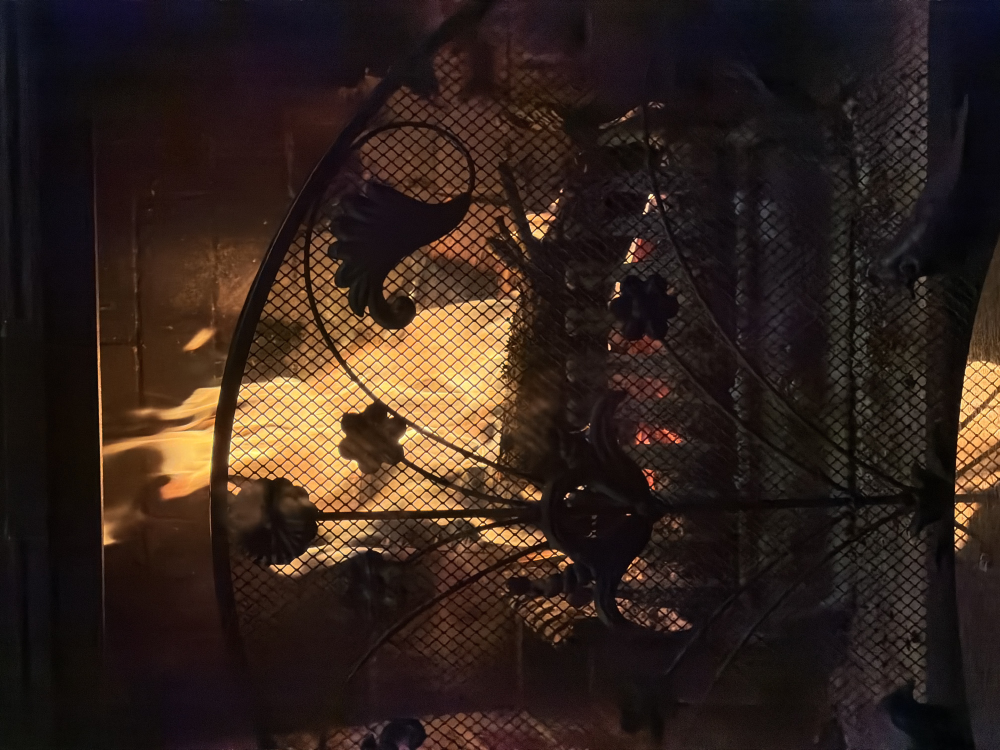 The image shows a fireplace with a decorative metal grate in front. The grate has floral-like designs. Behind the grate, flames are visible. The scene is dark, illuminated by the firelight. There is no information about the location of Кирково, Bulgaria within the picture.