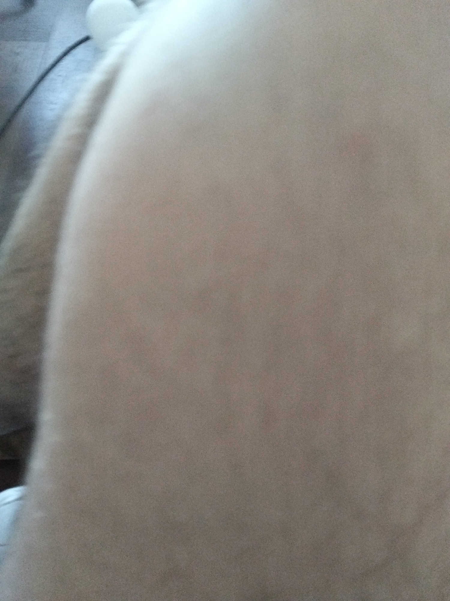 The image is a close-up of a person's leg, with a blurred background that appears to be an indoor setting. The lighting is dim, and the focus is primarily on the skin texture and a portion of fabric. There are no discernible objects or environmental features that would indicate a specific city or location. The scene is static and provides no information about any actions or interactions.