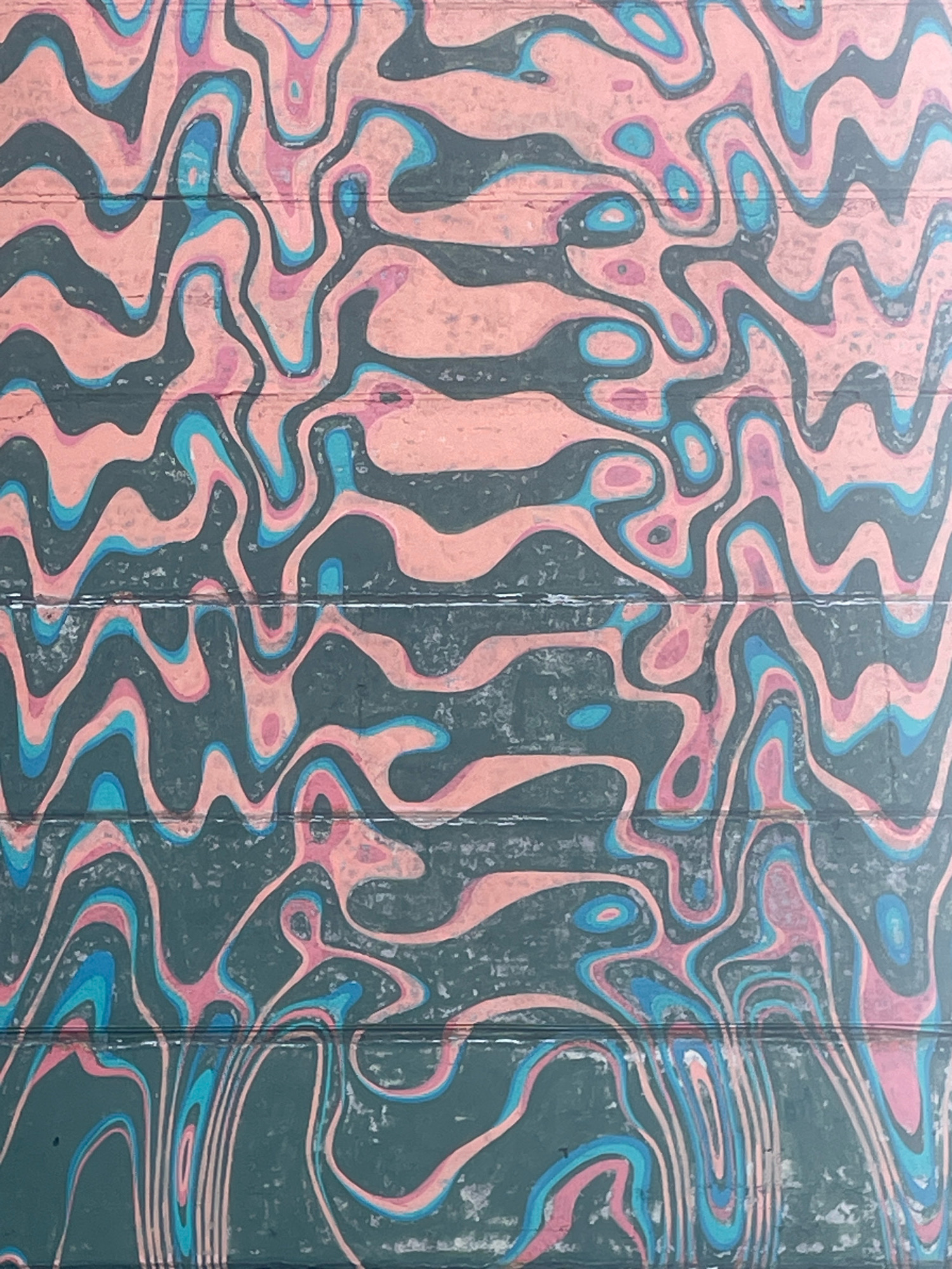 The image depicts a close-up, abstract view of a surface with a wavy, marbled pattern in shades of dark grey, salmon pink, and light blue. The pattern is consistent across the entire frame, with no discernible figures or objects. The texture appears somewhat rough, with visible lines or grooves running horizontally, suggesting it might be a wall, a textured fabric, or a painted surface with some imperfections. The lighting is even, with no strong shadows. There is no information in the image that suggests a specific location in Saint Petersburg, Russia, or any indication of people, actions, or interactions.