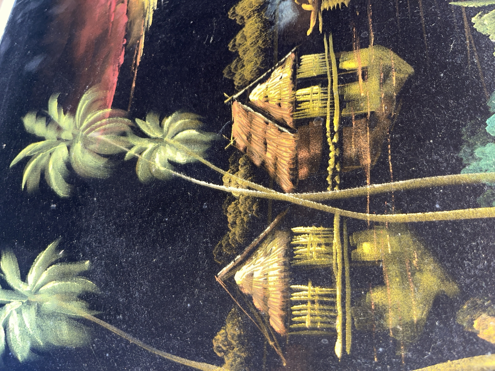 The image shows a detail of a painting, likely on a glossy surface. The painting depicts a tropical scene with palm trees on the left and two thatched-roof huts reflected in the water on the right. The huts are colored in shades of brown and yellow. The background is dark, likely black, with other painted elements in green, red, and yellow. The reflection of the huts and trees suggests a calm body of water. The style seems somewhat naive or folk art. There is no indication of the city of Tinaquillo, Venezuela.