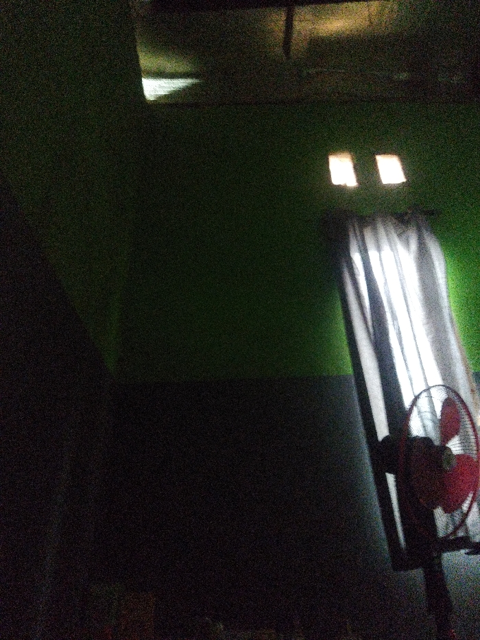 The image shows a dimly lit room with a ceiling fan and two windows covered with white curtains. The walls are painted a dark green color. The fan is on and rotating. There are no people in the room. The scene is located in a residential area in Subang, Indonesia, at coordinates -6.548 latitude and 107.766 longitude.