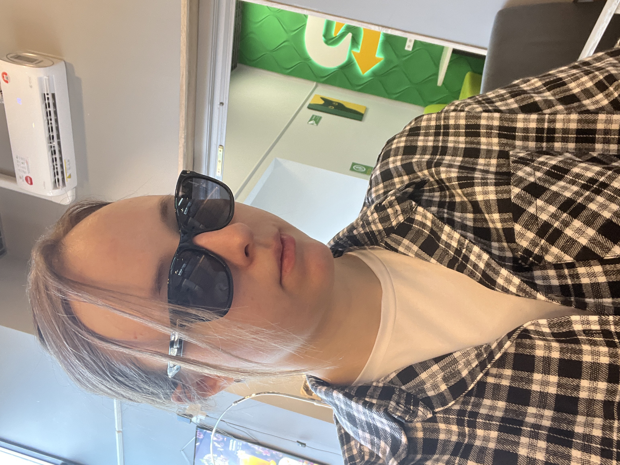 The image shows a person wearing sunglasses and a black and white checkered shirt, likely inside a Subway restaurant in Mytishchi, Russia, as evidenced by the Subway logo visible in the background. The person is also wearing a white shirt. A small, white air purifier is mounted on the wall. A television displaying an image is visible at the bottom of the frame.