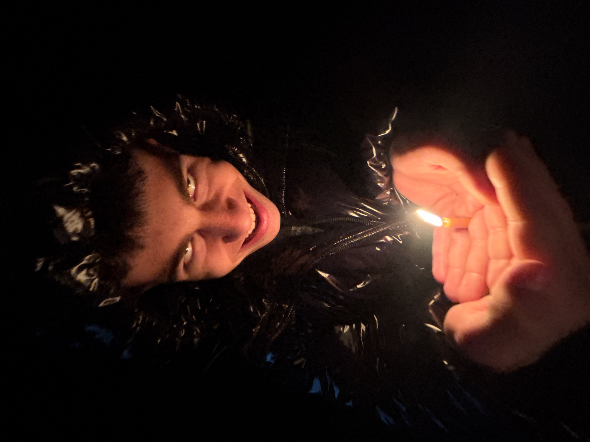 A man in a black, shiny jacket holds a lit lighter in his right hand, illuminating his face. He is smiling with visible teeth. The background is dark. There is no information about the location in Lehchevo, Bulgaria, in the image.