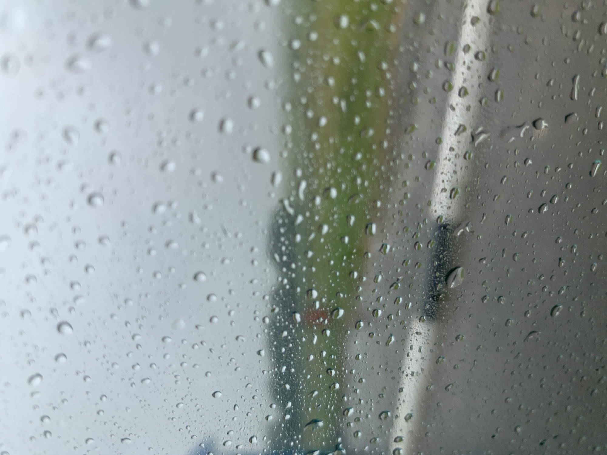 The image shows a close-up view of raindrops on a window, with a blurred outdoor scene in the background. The foreground is dominated by numerous water droplets of varying sizes, creating a textured and somewhat distorted view of what lies beyond.
In the background, a road with a white line is visible, suggesting it is a street or highway. Beyond the road, a green, grassy area is present, possibly a field or park. The sky appears overcast and gray, consistent with rainy weather. There are no people or specific identifiable structures visible in the cropped portion of the background. The overall impression is a serene, yet slightly melancholic, scene of a rainy day.
The location provided, Курапольскі сельскі Савет, Belarus, suggests a rural or semi-rural area within Belarus. This context aligns with the observed elements of a road, fields, and the absence of dense urban development. The weather conditions depicted are typical of various regions during periods of rainfall.