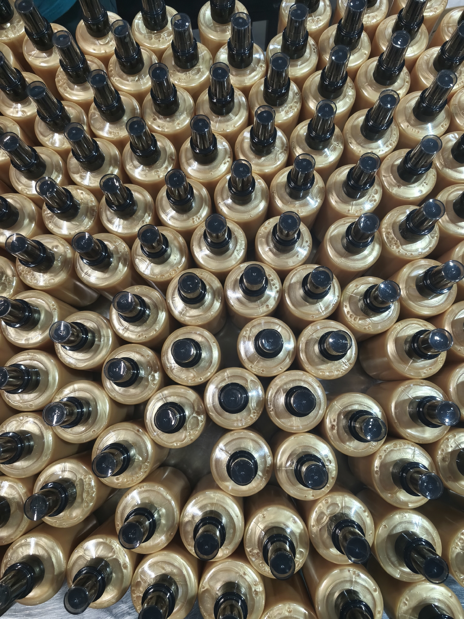 The image shows a large number of cylindrical, gold-colored bottles with black spray nozzles. The bottles are densely packed together, oriented vertically. The scene is likely indoors, given the controlled lighting and orderly arrangement of the bottles. There is no indication of the location being in the city of Сокуры, Russia. There are no people visible in the frame. The primary objects are the bottles, and the action implied is their storage or packaging, though the precise context is unclear from the image alone.