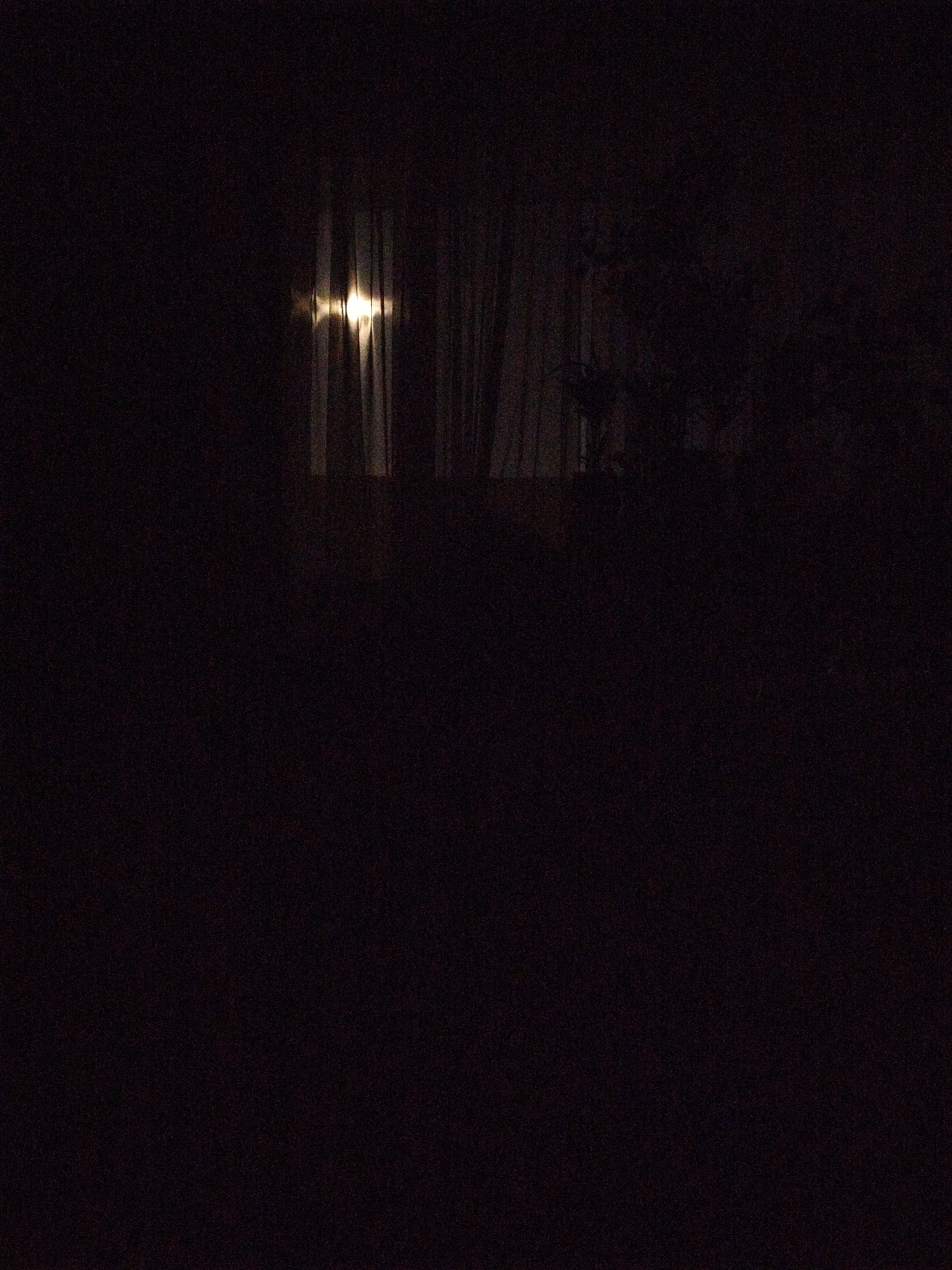 A dark image shows a window with light shining through curtains, possibly in Sofia, Bulgaria, though the location is unverifiable. The rest of the image is obscured by darkness, making it difficult to discern any other subjects or objects.