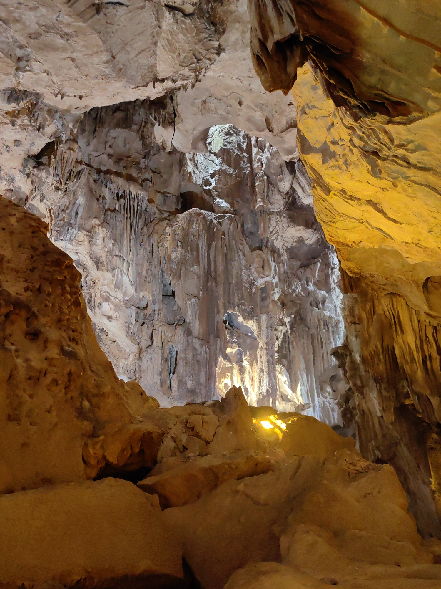 The image depicts a view inside a cave located in Lạng Sơn, Vietnam. The cave features various rock formations, including stalactites and stalagmites, illuminated by warm, artificial lighting. The rock surfaces exhibit a range of colors from light beige to yellow. The overall perspective is looking upwards, emphasizing the height and complexity of the cave interior. No people are visible in the scene.